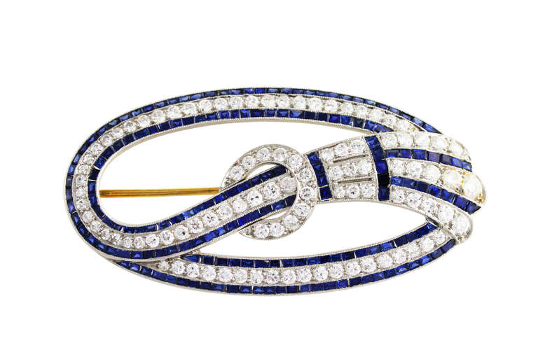 An Art Deco platinum, sapphire and diamond brooch of fabulous workmanship by Tiffany & Co., of openwork oval shape designed as a stylized ribbon gathered in the center, set throughout with 97 old European-cut diamonds weighing approximately 3.50