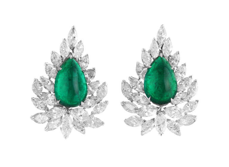 This stunning pair of earclips are set in the centers with 2 very clear and deep green pear-shaped cabochon emeralds weighing 14.09 carats, which measure approximately 15.8 by 10.9 by 6.5 mm. and 16.1 by 10.7 by 6.7 mm., then framed by 44