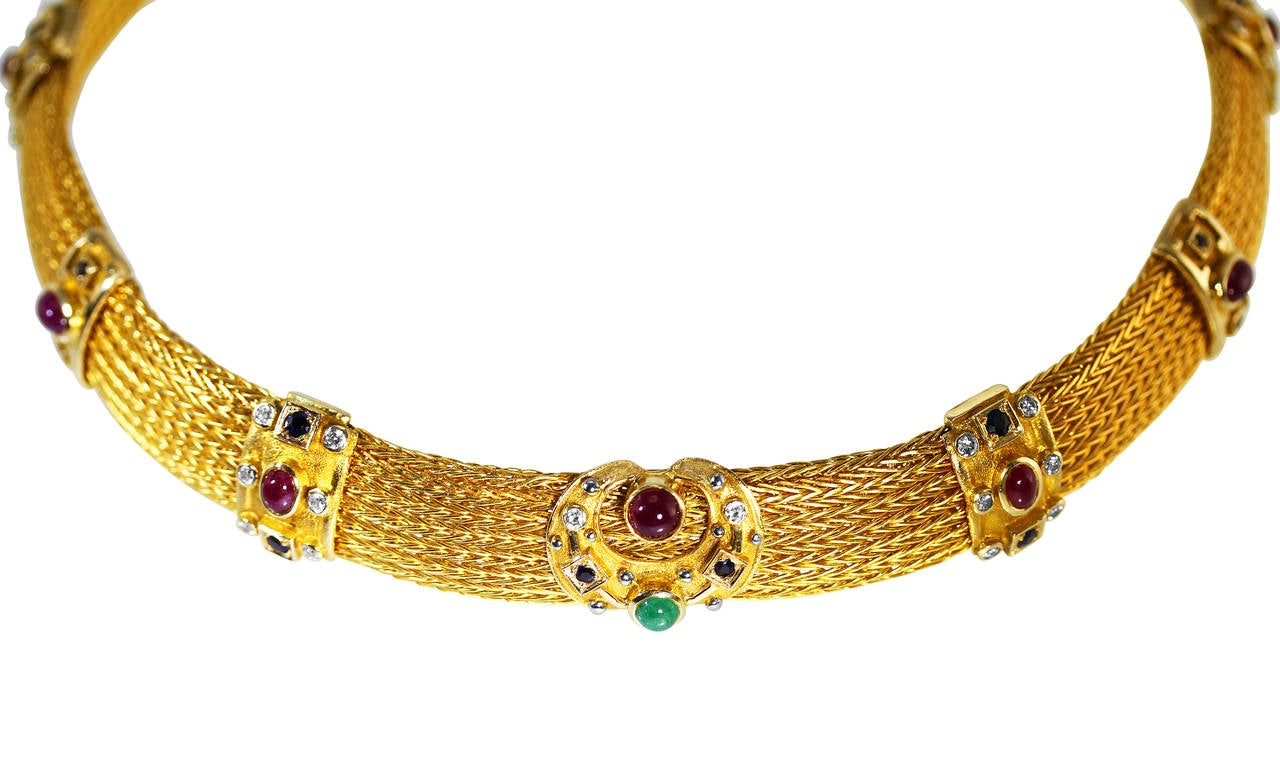 An 18 karat gold, ruby, emerald, sapphire and diamond necklace by Lalaounis, Greece, the wide gold mesh strap set with 10 plaques set with 10 oval and round cabochon rubies weighing approximately 5.20 carats, 20 round sapphires weighing