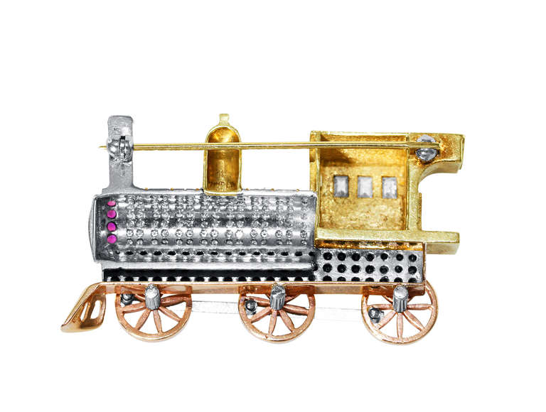 A whimsical 18 karat yellow, pink and white gold, diamond and ruby locomotive brooch, the train of tri-colored gold design set with 98 white diamonds weighing approximately 1.00 carat, the windows set with 3 emerald-cut diamonds weighing
