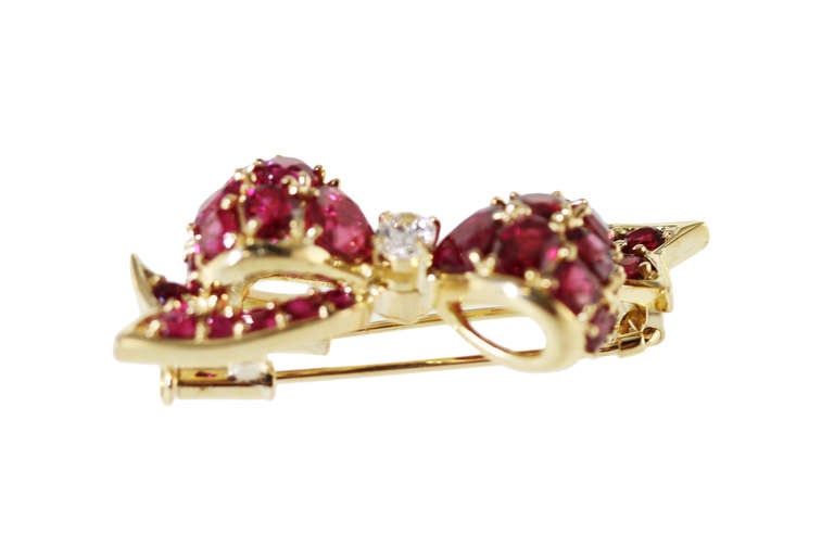 A lovely 18 karat yellow gold ruby and diamond bow brooch, of stylized design set in the center with an oval diamond weighing 0.33 carat, the bow set with 5 oval, 18 round and 8 pear-shaped rubies weighing approximately 6.00 carats, gross weight