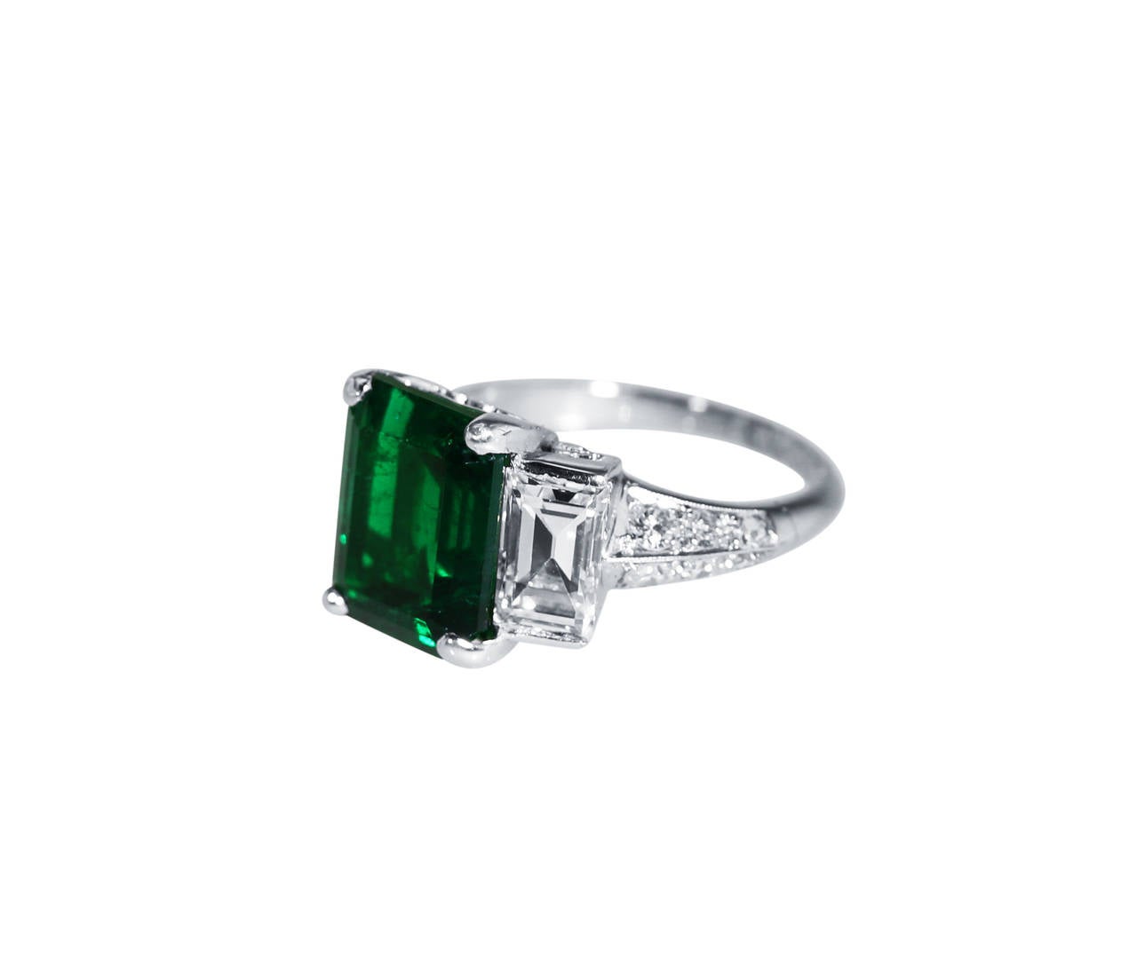 A platinum, emerald and diamond ring, set in the center with an emerald-cut emerald weighing 4.64 carats, flanked by 2 larger baguette diamonds weighing approximately 2.00 carats and  22 round diamonds weighing approximately 0.40 carat, size 6,