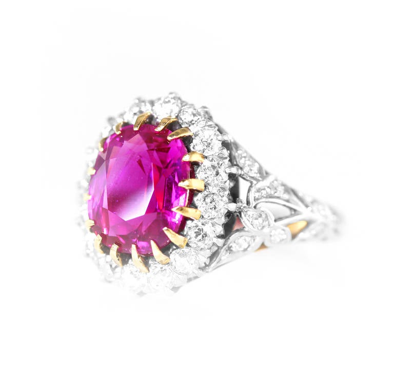 An antique 18 karat gold, platinum, ruby and diamond ring, set in the center with an oval ruby weighing 4.42 carats, framed by 16 old European-cut diamonds weighing approximately 0.65 carat, flanked by a tapered band of foliate design set with 16