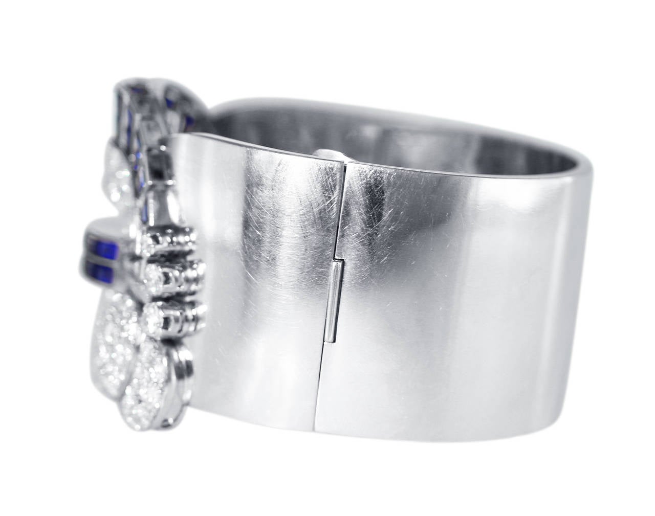 An Art Deco platinum, sapphire and diamond cuff bracelet, the hinged cuff set at the front with an ornate plaque of scrolls and fans set throughout with 42 square-cut sapphires weighing approximately 11.00 carats, accented by 112 old European-cut