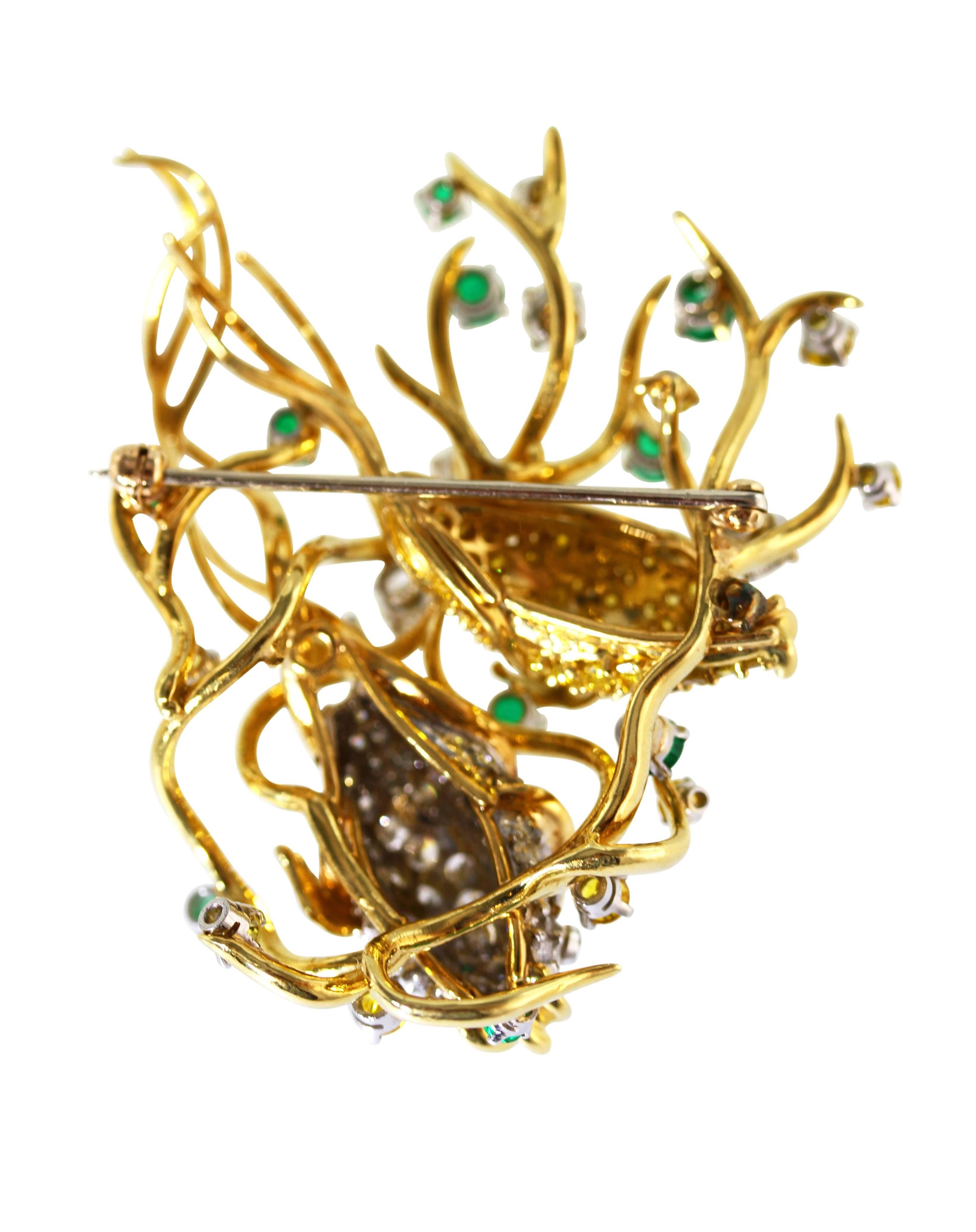 An 18 karat yellow gold, diamond, emerald and colored diamond fish brooch, designed as two fish among gold water-like tendrils set throughout with 64 white diamonds weighing approximately 4.00 carats, 63 yellow diamonds weighing approximately 3.95