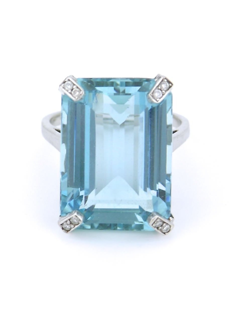 An emerald cut aquamarine of 19cts of very good colour intensity and clarity. Four claw set in 18k white gold with small diamonds mounted into the claws over a pierced and fretted gallery of scrolls.

Currently size N (USA 6 1/2), please enquire