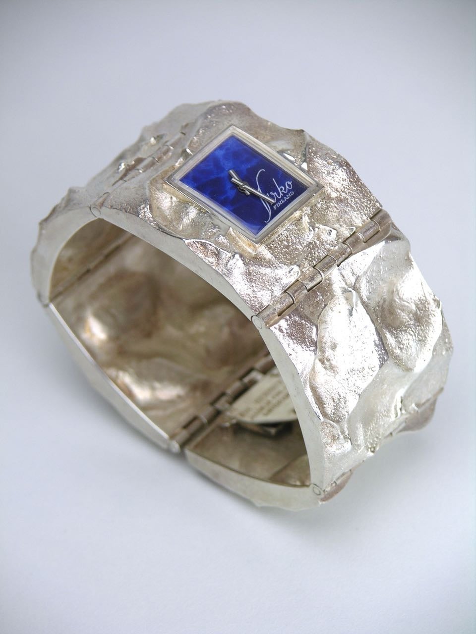 A wonderfully wide topographical textured heavy panel bracelet set with a small square manual watch with a lapis blue enamel face 

- a continuation of the Moon Jewellery series which was inspired by the photographs and information coming back