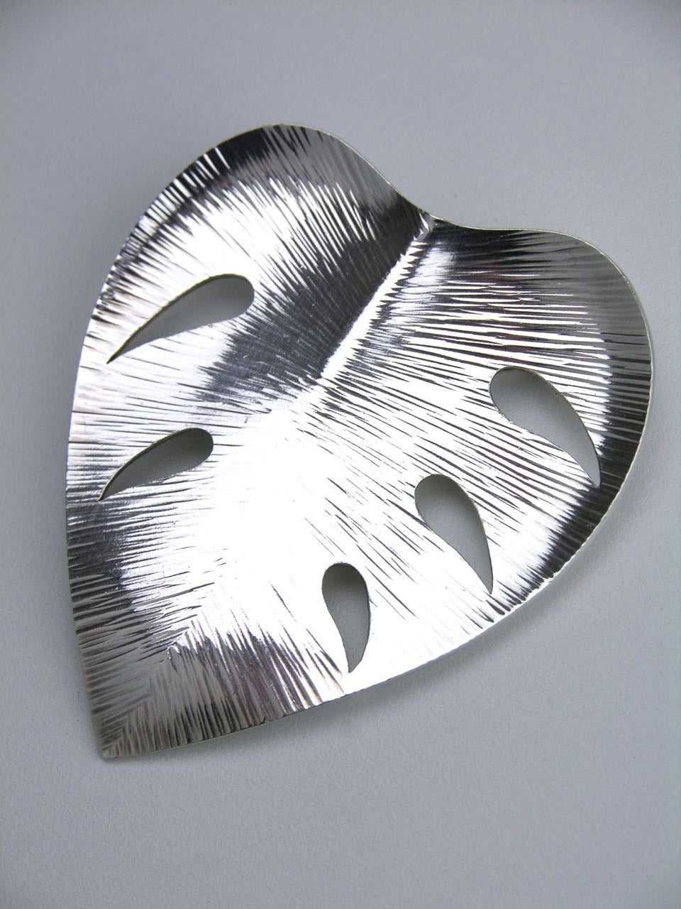 A large slightly concave leaf shape with a raised fold in the centre, apertures and a textured finish with a rollover clasp to the pin placed diagonally at the back

- marked Sterling and marks for Eigil Jensen of Anton Michelsen, the Jewellers to