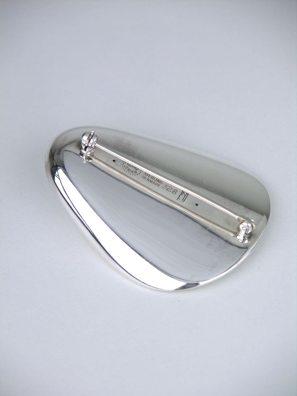 A streamlined elliptical brooch of a modernist concave thumbprint shell type motif with a roll over clasp to the pin on the back 

- marked with post 1945 marks for Georg Jensen of Copenhagen and for design number 328 by Nanna and Jorgen Ditzel
