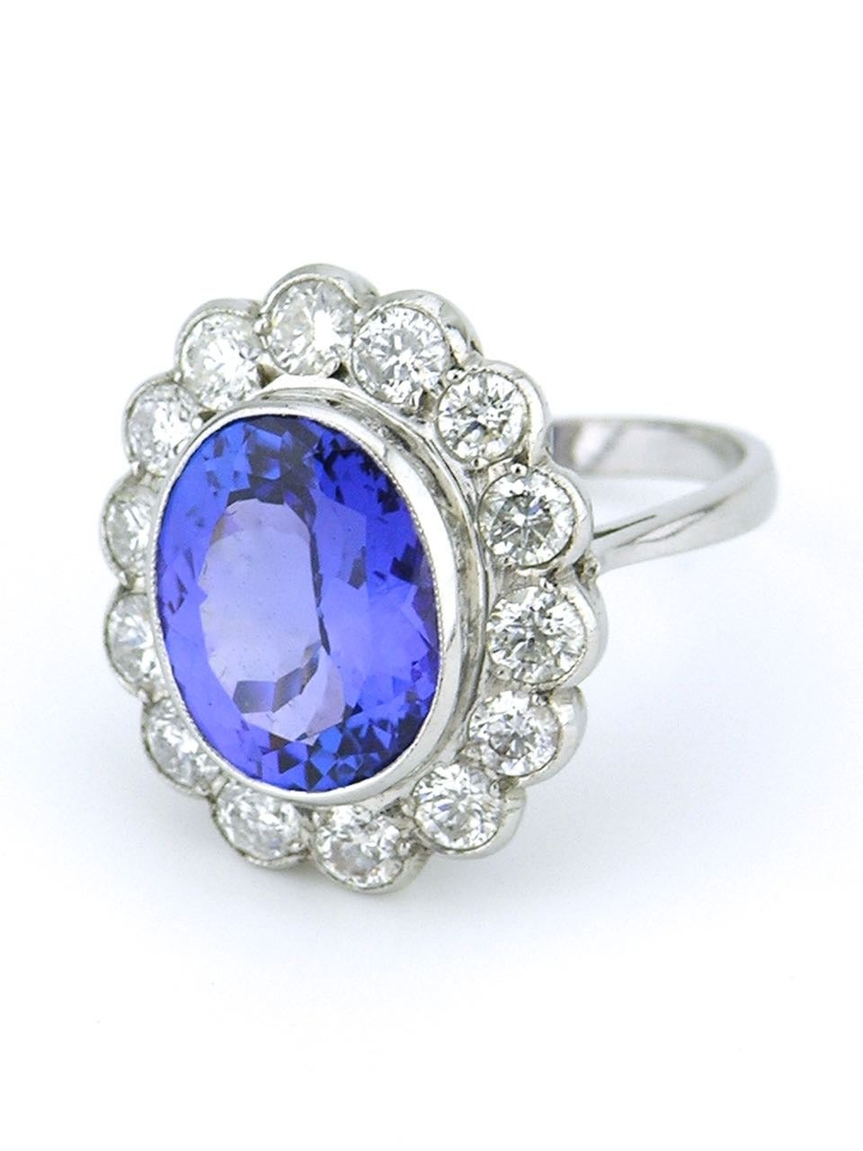 A diamond and tanzanite ring consisting of a bezel set oval tanzanite of intense medium violet blue colour approx 6cts surrounded with 14 brilliant cut diamonds totalling approx 0.80ct in an 18ct white gold setting 

- total weight 8grms 
-