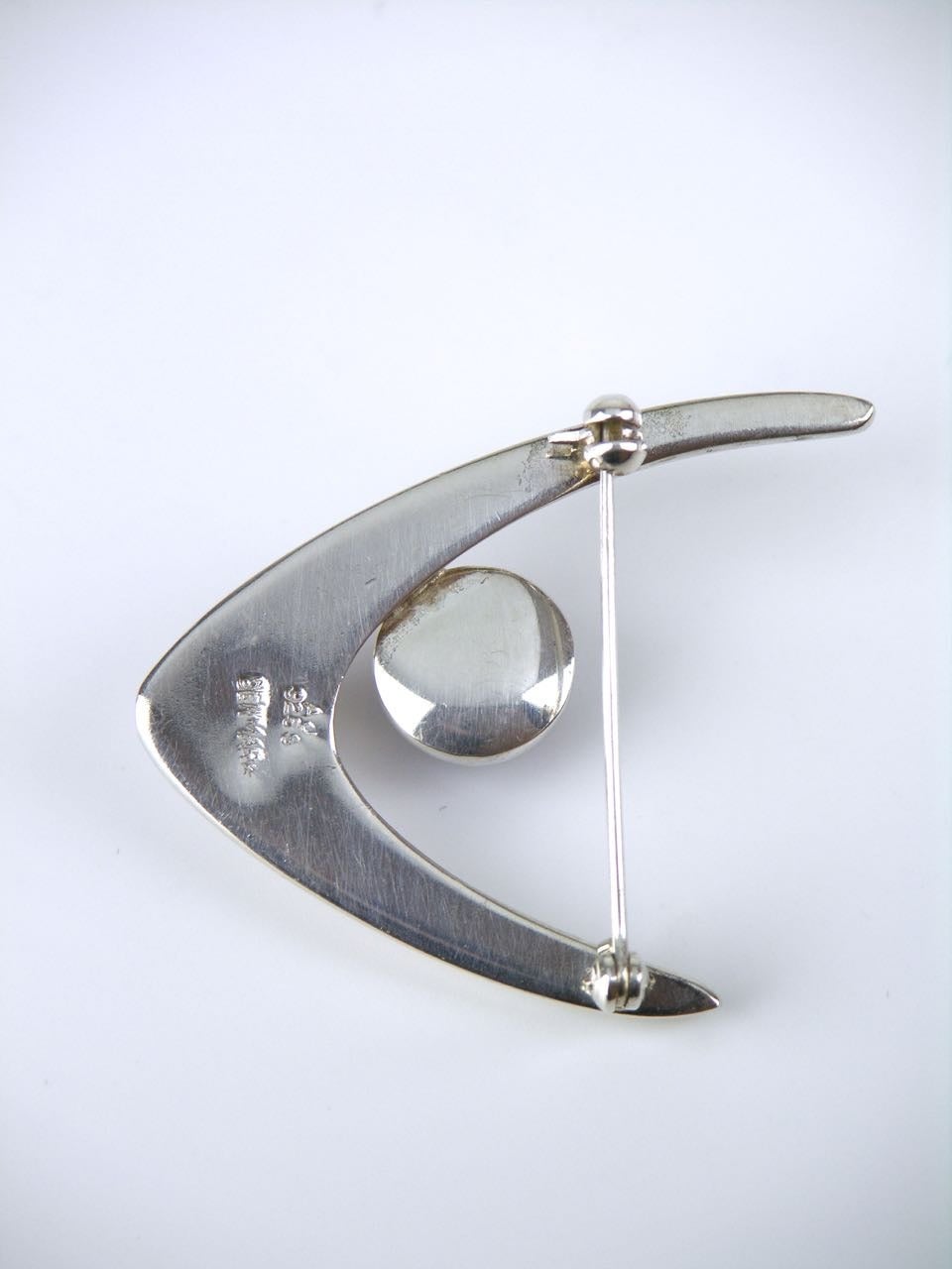 A solid silver and cabochon amethyst wishbone motif brooch consisting of a wishbone shape with a cabochon amethyst bezel set and suspended in between the arms fitted with with a rollover safety clasp to the pin on the reverse.

- marked AJ for