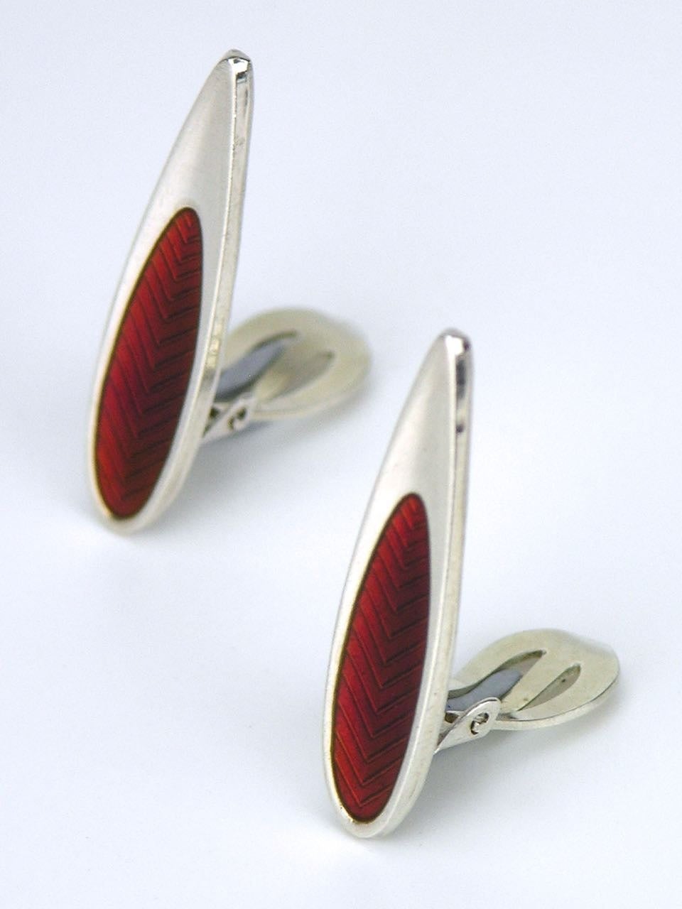 A pair of solid silver and red enamel modernist teardrop shape clip earrings; each earring consisting of a slightly concave elongated leaf shape with a smaller panel of red enamel over a chevron guilloche pattern and a clip fitting to the