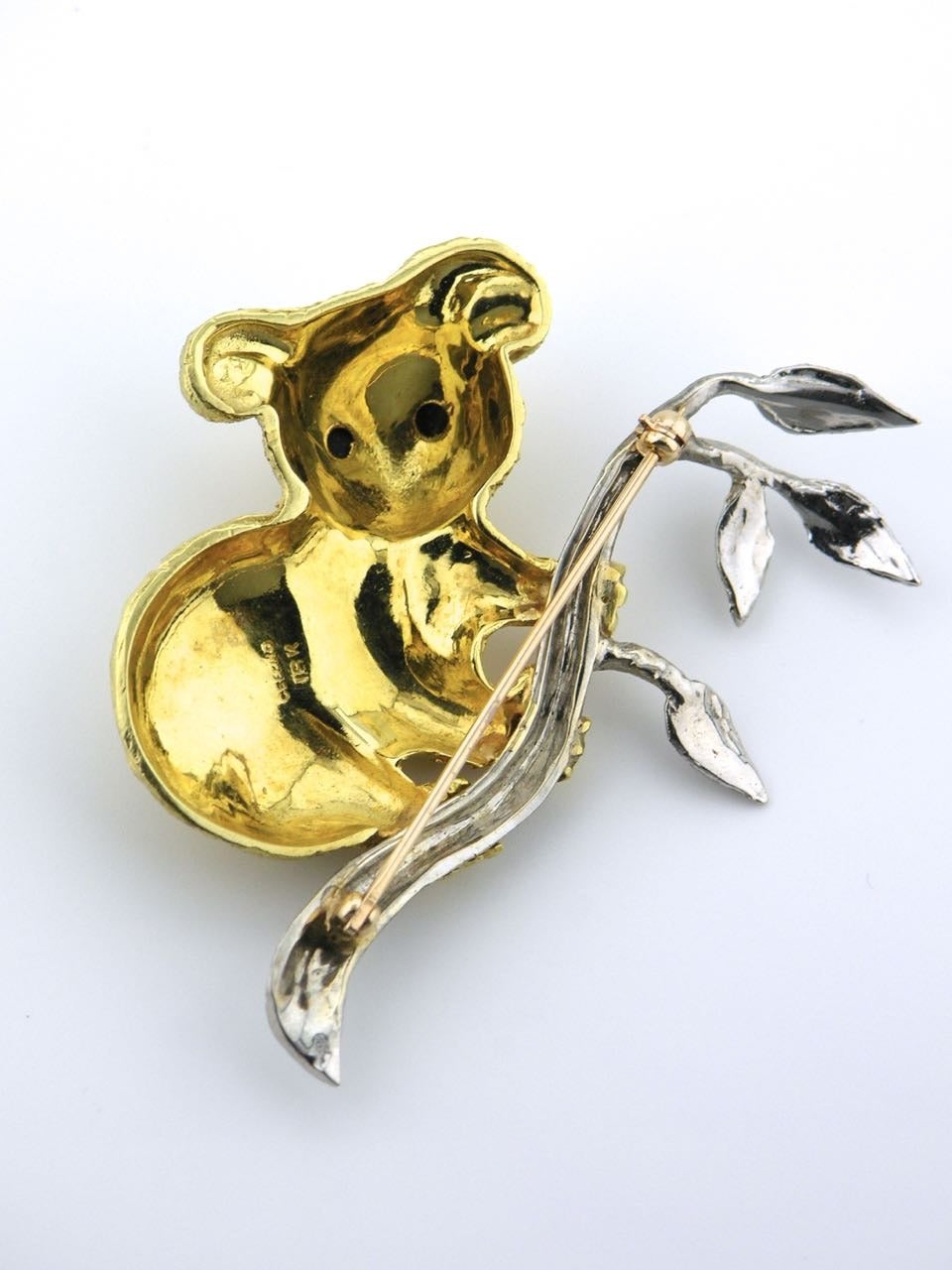 An 18kt yellow and white gold Koala pin - a yellow gold Koala with onyx eyes sitting on a white gold branch with leaves 

- marked Cellino 18k 
- total weight 27.6grms 
- overall dimensions 60 x 60 mm 
- c.1980 Italy