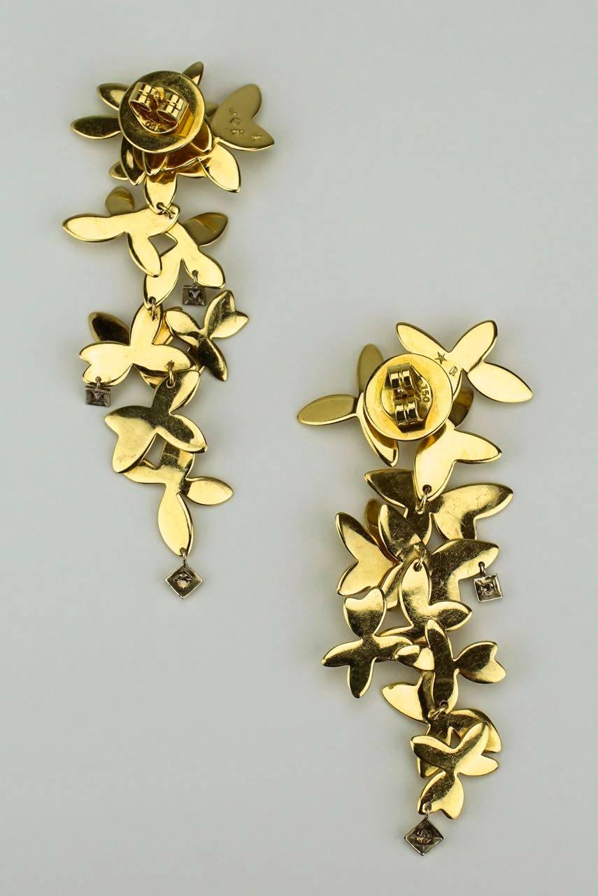A pair of 18k yellow gold cascading flower drop earrings - each earring consisting of abstract silhouettes of floral motifs hinged and layered to form a tapered drop earring - accented with small bezel set princess cut champagne diamonds (3 on the