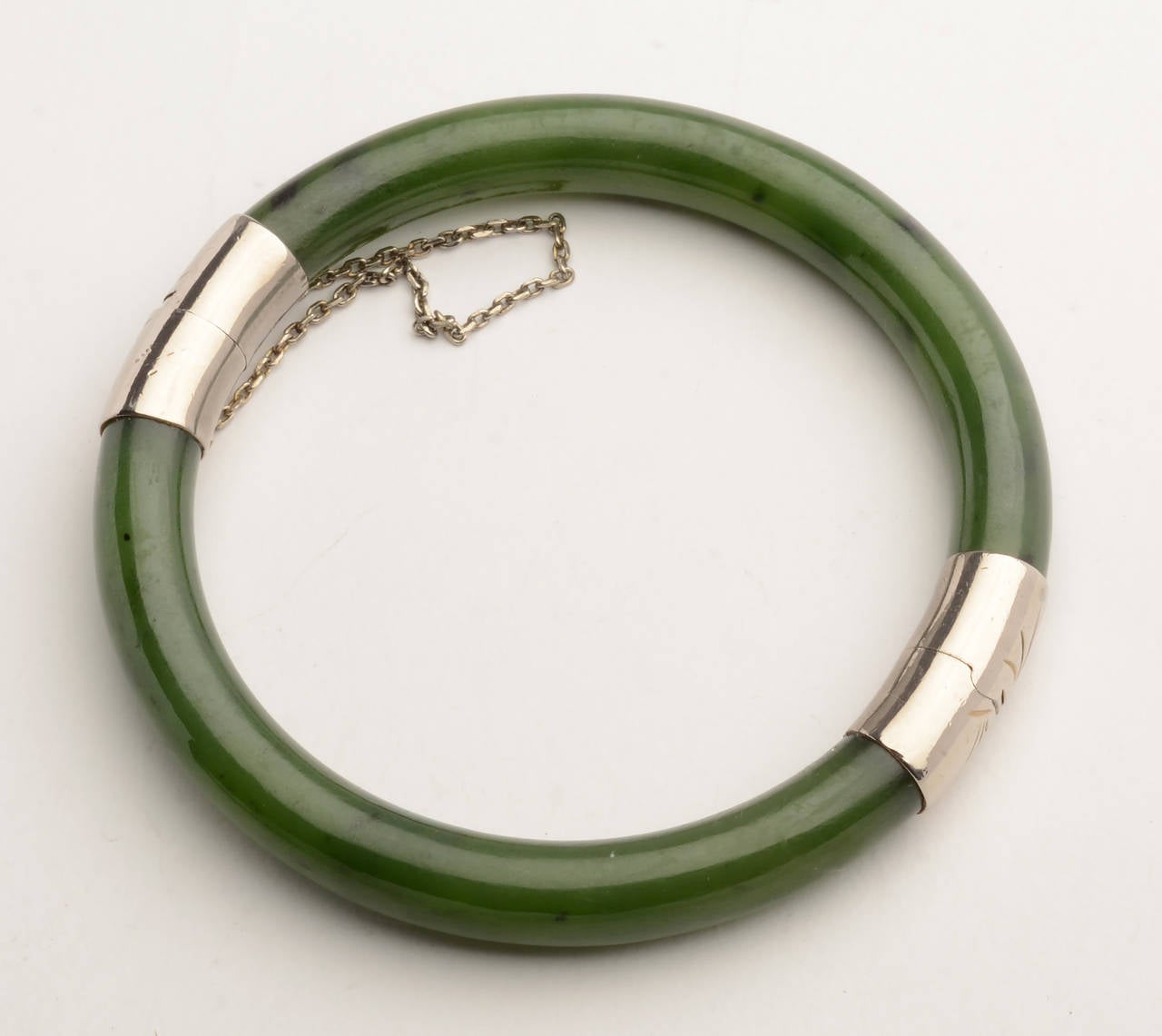 Richly colored nephrite bangle bracelet with two sterling silver ornaments. Both are incised with stylized leaf motifs. The interior diameter is 2 3/16