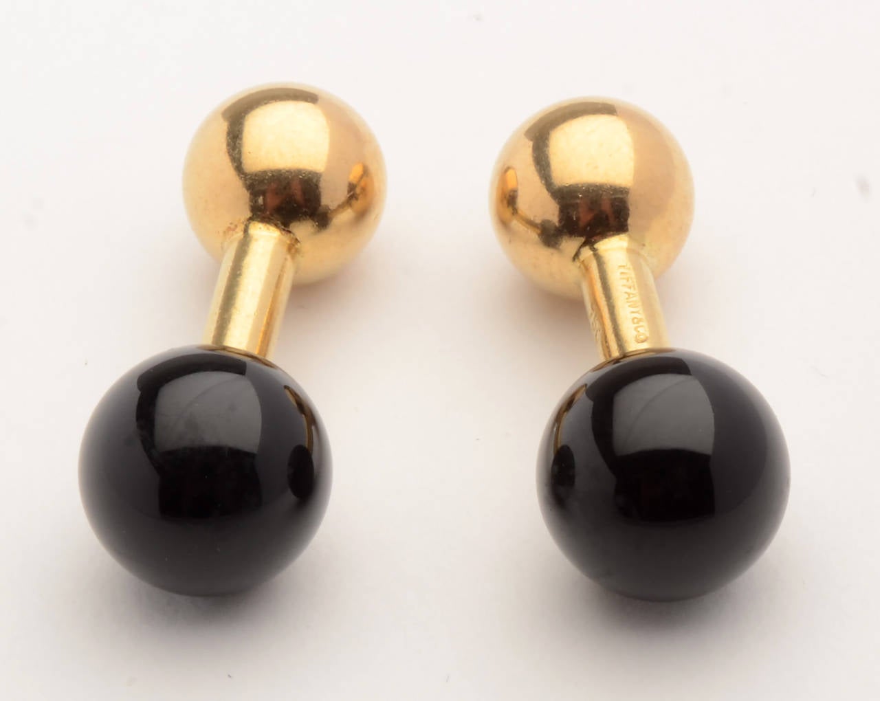 Classic 18 karat gold barbell cufflinks by Tiffany and Co. with a black onyx ball reversing to a gold one. The onyx is 7/16