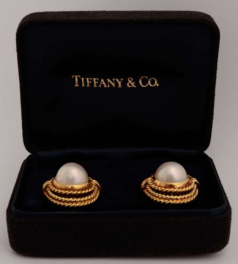 Tiffany 18 karat gold earrings centered with a 12 mm mabe pearl. Each pearl is surrounded by a round band of twisted gold and two gold ovals. Measurements are 13/16