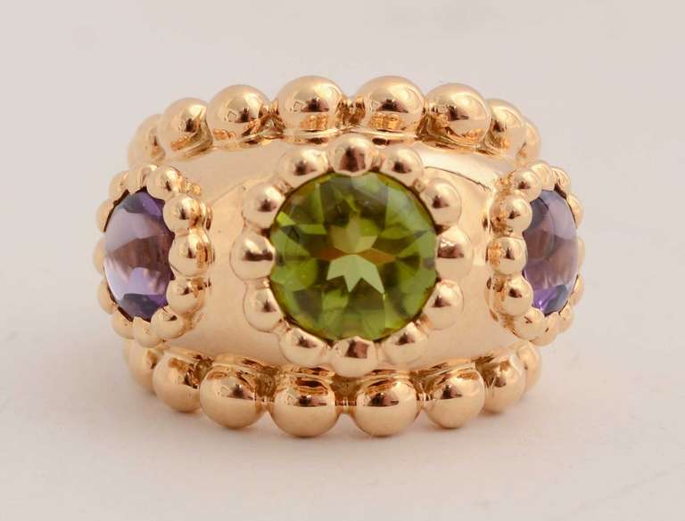 Stunning 18 karat gold domed ring by Chanel with a central peridot flanked by amethyst on either side. Gold beading surrounds the stones as well as the band of the ring. It is size 5 1/4.