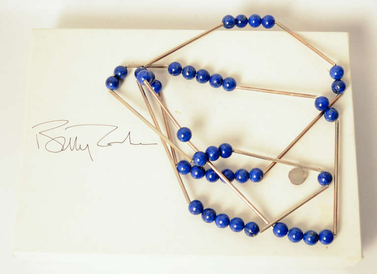 This long sterling and lapis lazuli necklace is classic Betty Cook- streamlined and airy. It is made of silver tubes with round lapis beads alternating from groups of one to six throughout the 36 inch length. 
The necklace is sold in its original