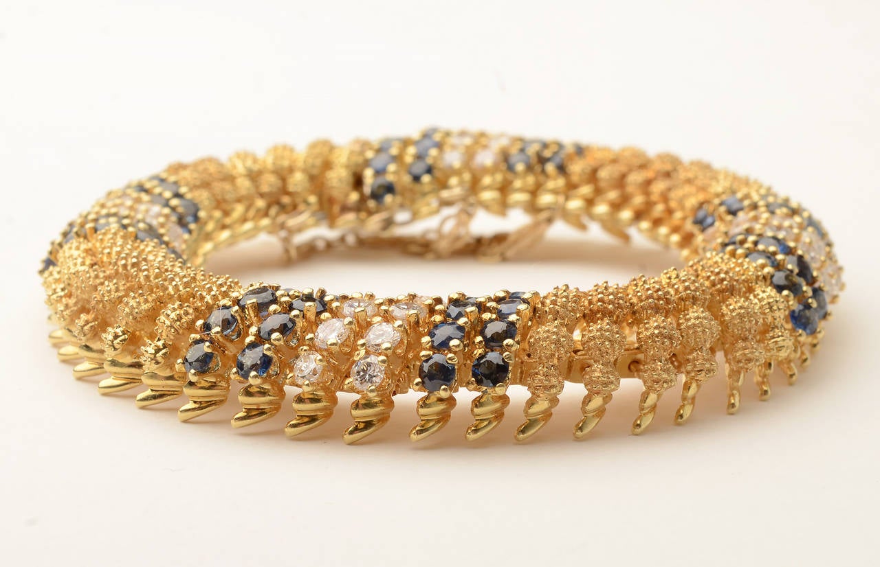 Elegant and intricate gold bracelet enhanced with diagonal bands of sapphires and diamonds. The round gold links are nicely textured. The bracelet has 40 brilliant cut diamonds weighing 3.5 carats.  80 round sapphires weigh 8.2 carats. The bracelet