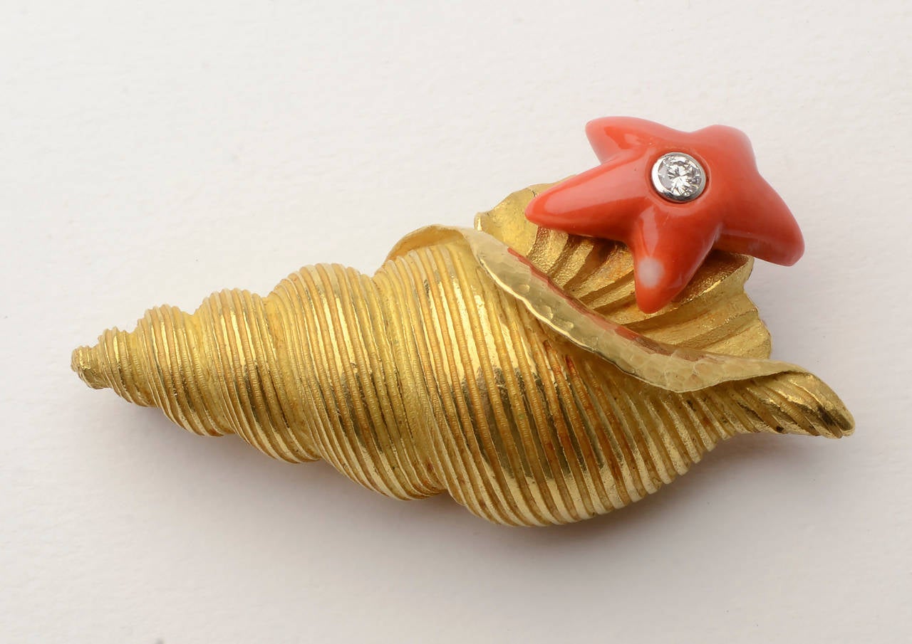 Stunning and unusual gold seashell from which a coral starfish emerges. The starfish is centered with a diamond. The shell is beautifully textured. It measures 2 9/16