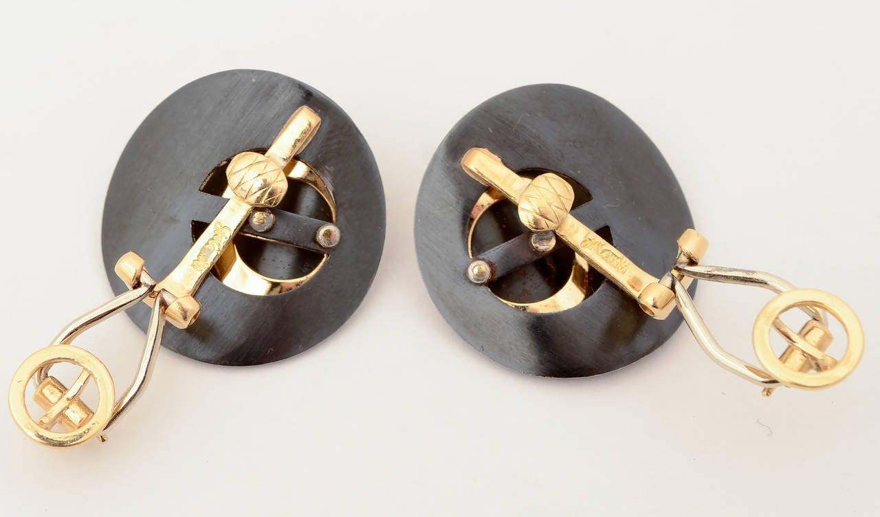These Modernist looking earrings consist of three concave circles. The center is gold with blackened steel above and below. The widest is 1 inch in diameter. Backs are clips. They are designer signed but difficult to decipher. The name may be