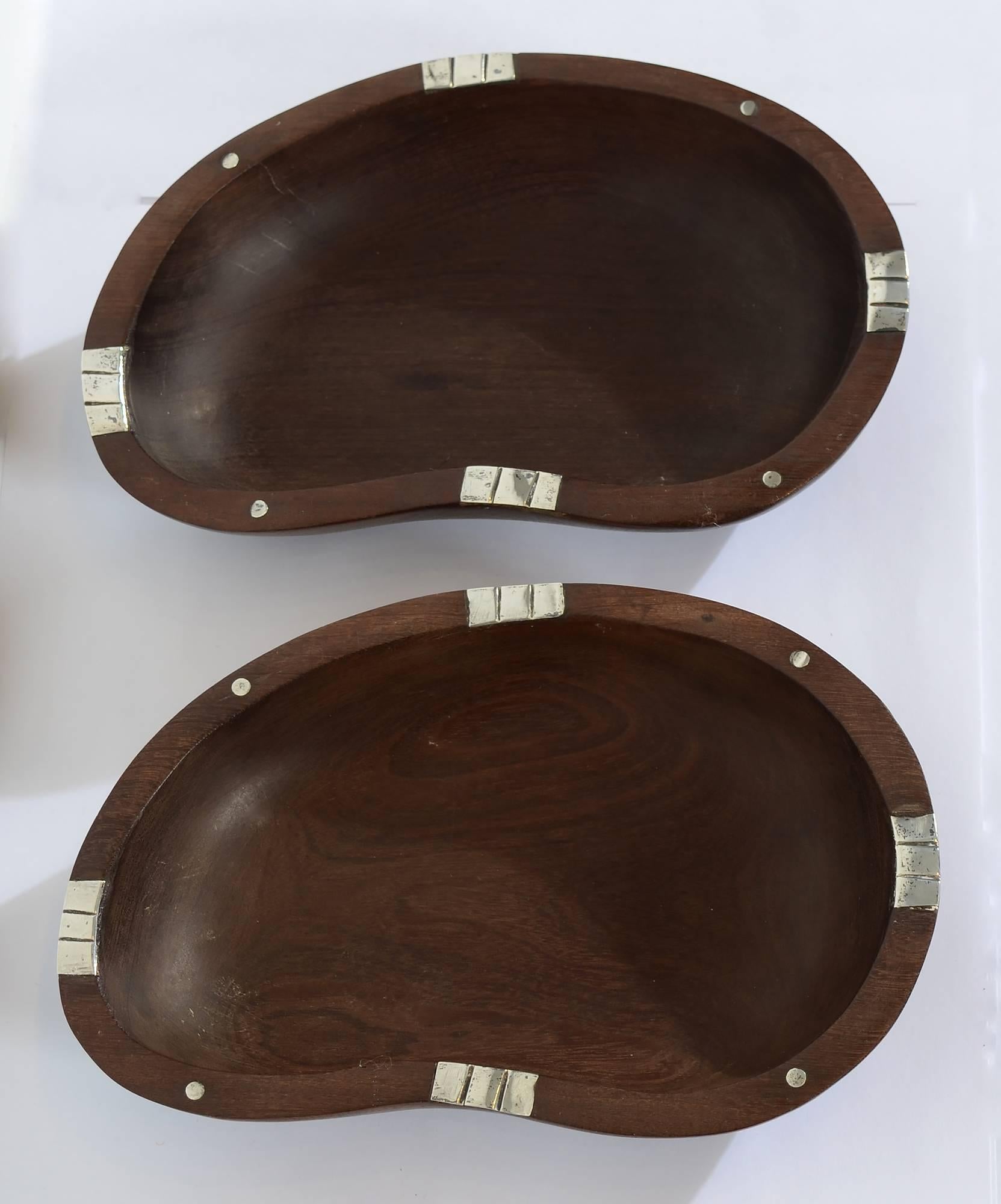 This is an unusual pair of wood bowls by silver master, William Spratling. The wood bowls have silver ornamentation of squares and circles. The lima bean shaped bowls measure 7