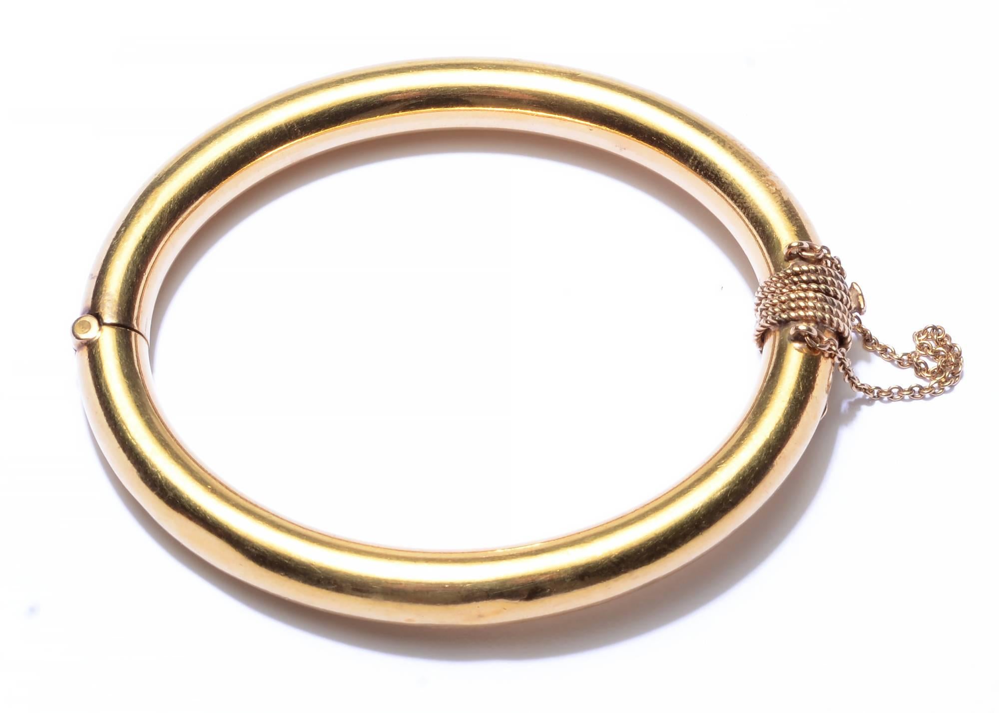 This tubular, hinged gold bangle bracelet is substantial in size and weight. The circumference of the metal is 1 inch. The bracelet weighs 40 grams. The clasp is wrapped with six rows of twisted gold. It has both clasp and chain safetys. The gold