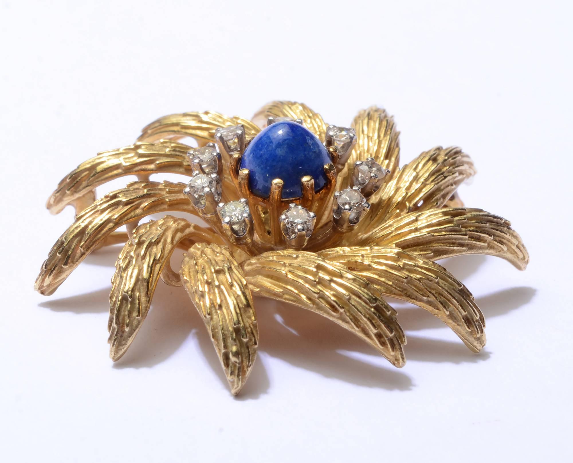 This swirling floral brooch by La Triomphe is wonderful with texture and color. Each petal has a layered appearance to the surface. A central round lapis lazuli is surrounded by nine diamonds. The brooch measures 1 3/8