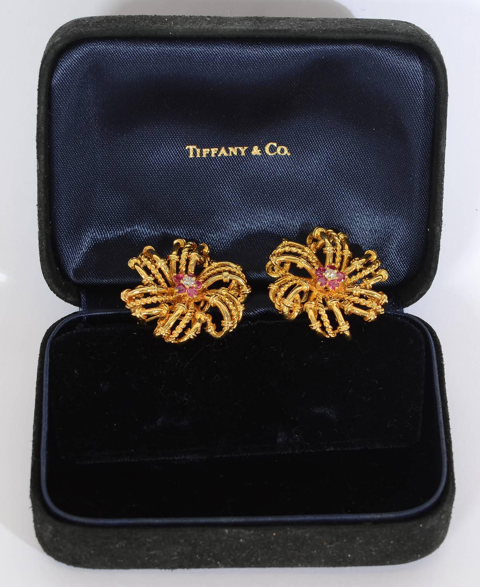 Tiffany 18 karat earrings with six swirling arms. Each arm is made of three loops  - the center is twisted gold and smooth with bands on either side. The center of each earring is a diamond surrounded by five rubies.also giving the effect of a star.