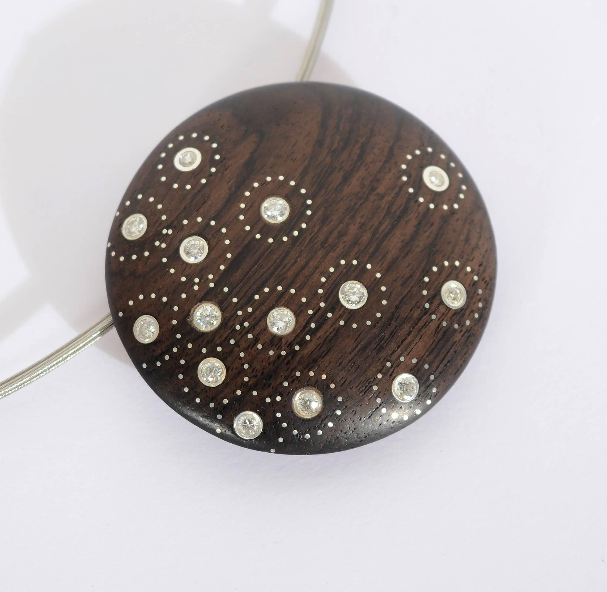 Fourteen diamonds are set in ebony in this unusual pendant necklace. Tiny inlaid silver dots surround each diamond. The pendant is strung on 5 strands of steel cable measuring 16 1/2 inches long. Total diamond weight approximately .7 carats.