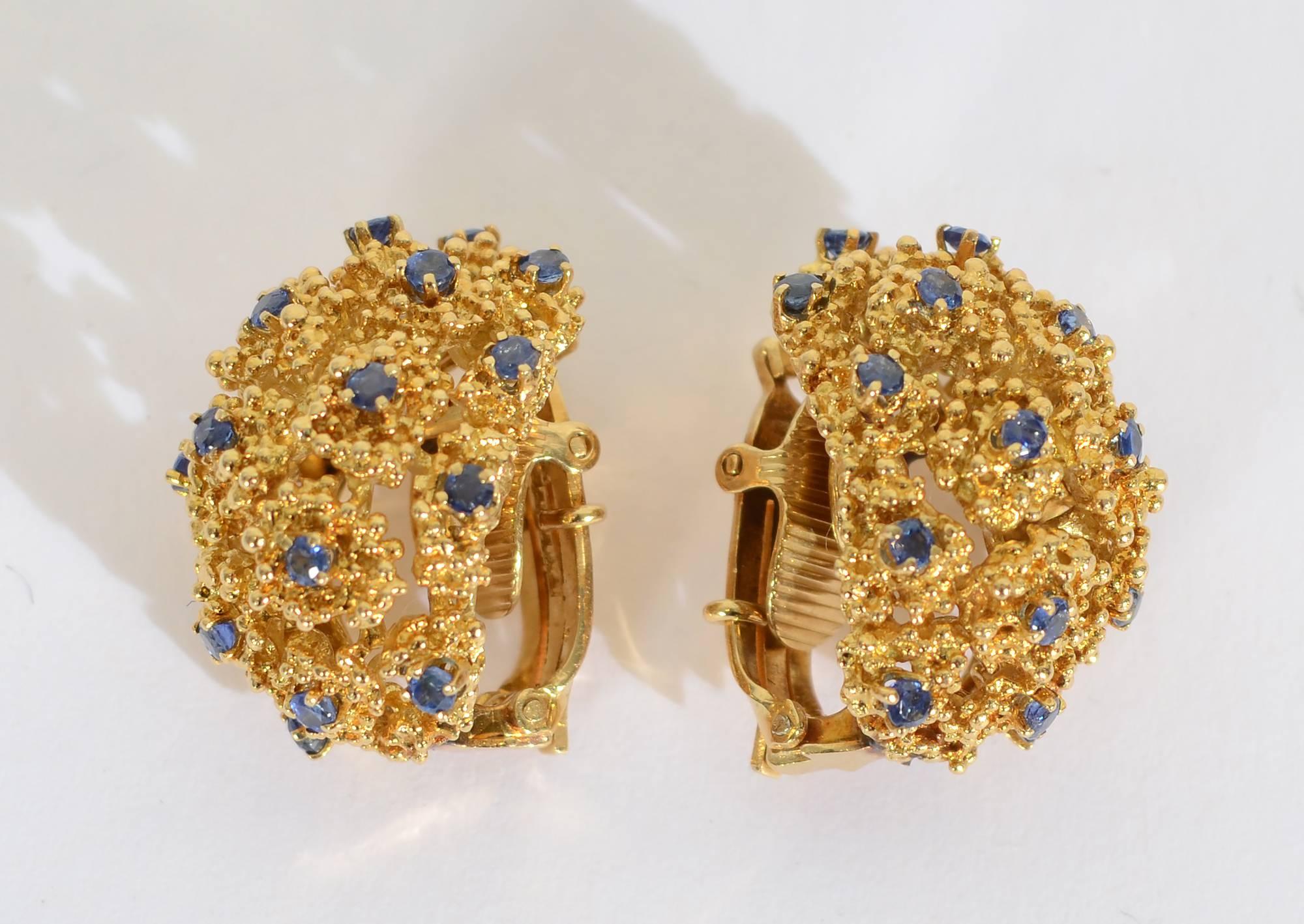 Tiffany half round  earrings with sapphires surrounded by clusters of heavily textured irregular circles. The earrings are 18 karat gold. Clip backs can be converted to posts. They are 1 inch long and 3/4 
