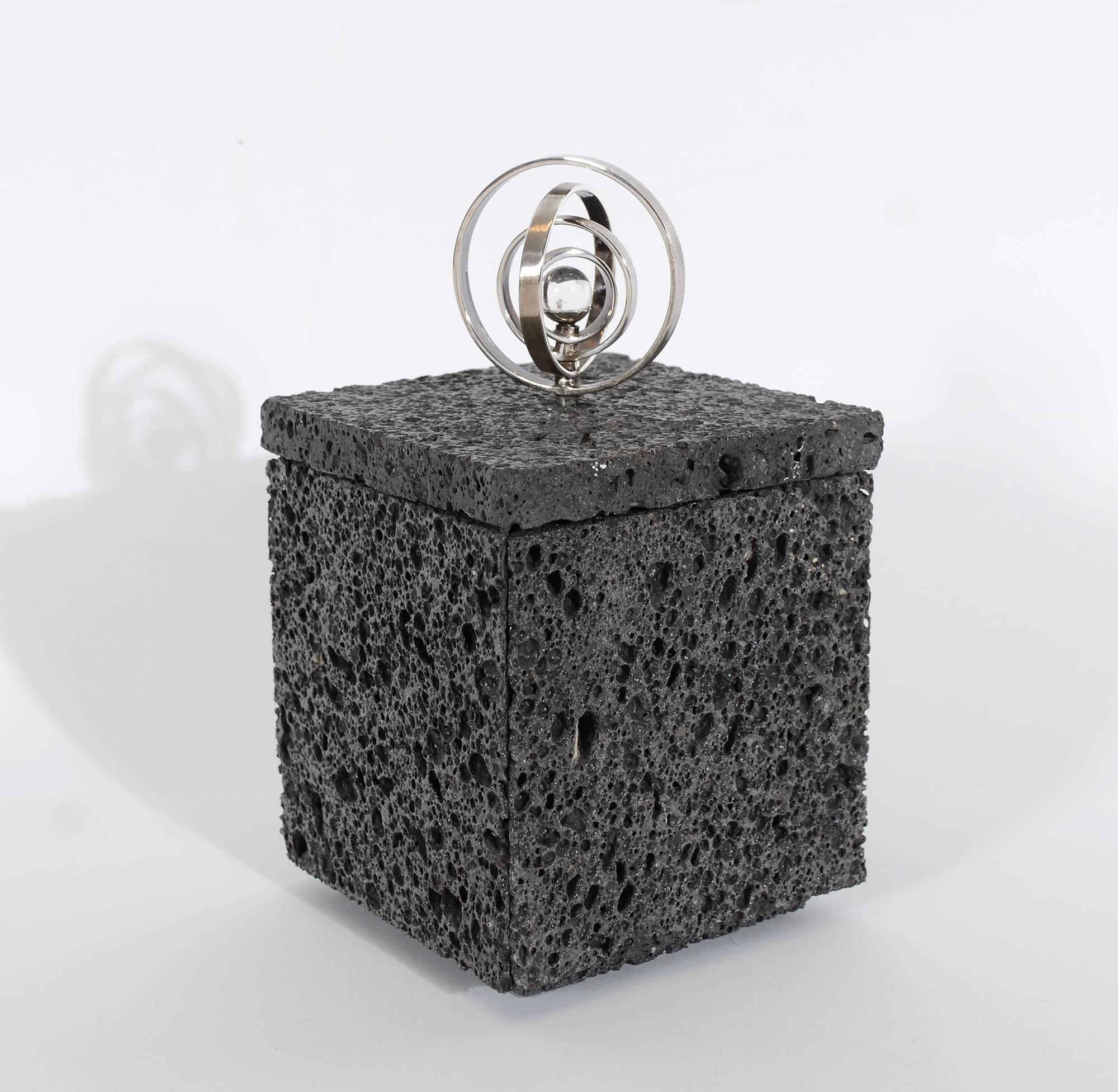 This box made of volcanic lava is topped with a sterling silver and crystal ball finial. The four silver circles are movable to create either a flat or three dimensional form. The interior of the box is lined with red leather. The box measures 3 1/8