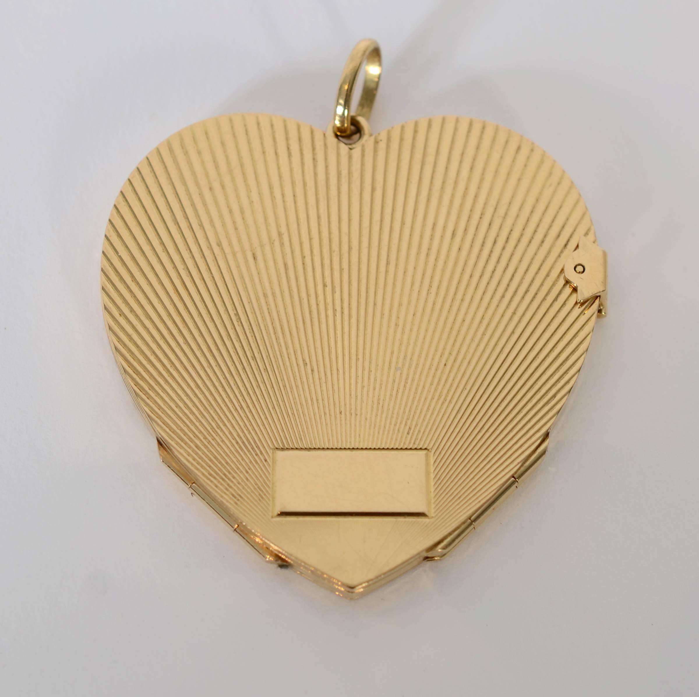 This 18 karat gold Retro heart locket is unusual in two ways. It is larger than most at 2 inches in length and width and it opens to four compartments rather than the usual two. The back has a rectangular plaque that can be engraved. Textured lines