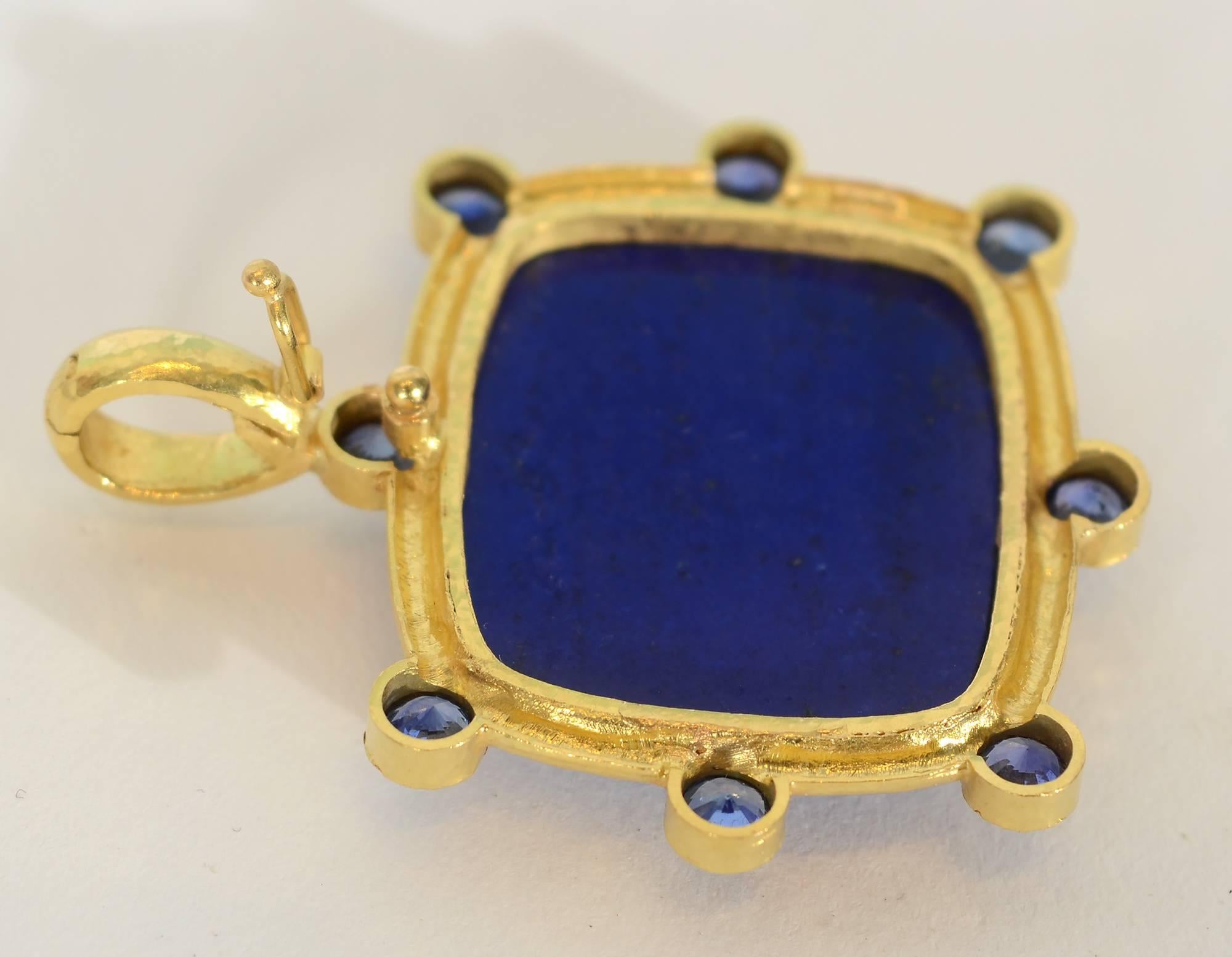 Striking pendant by Elizabeth Locke with an intensely colored central lapis lazuli. Surrounding the rectangular stone are eight fine sapphires. The frame around the stones is done in Locke's signature hammered gold finish. The piece is 1 9/16"