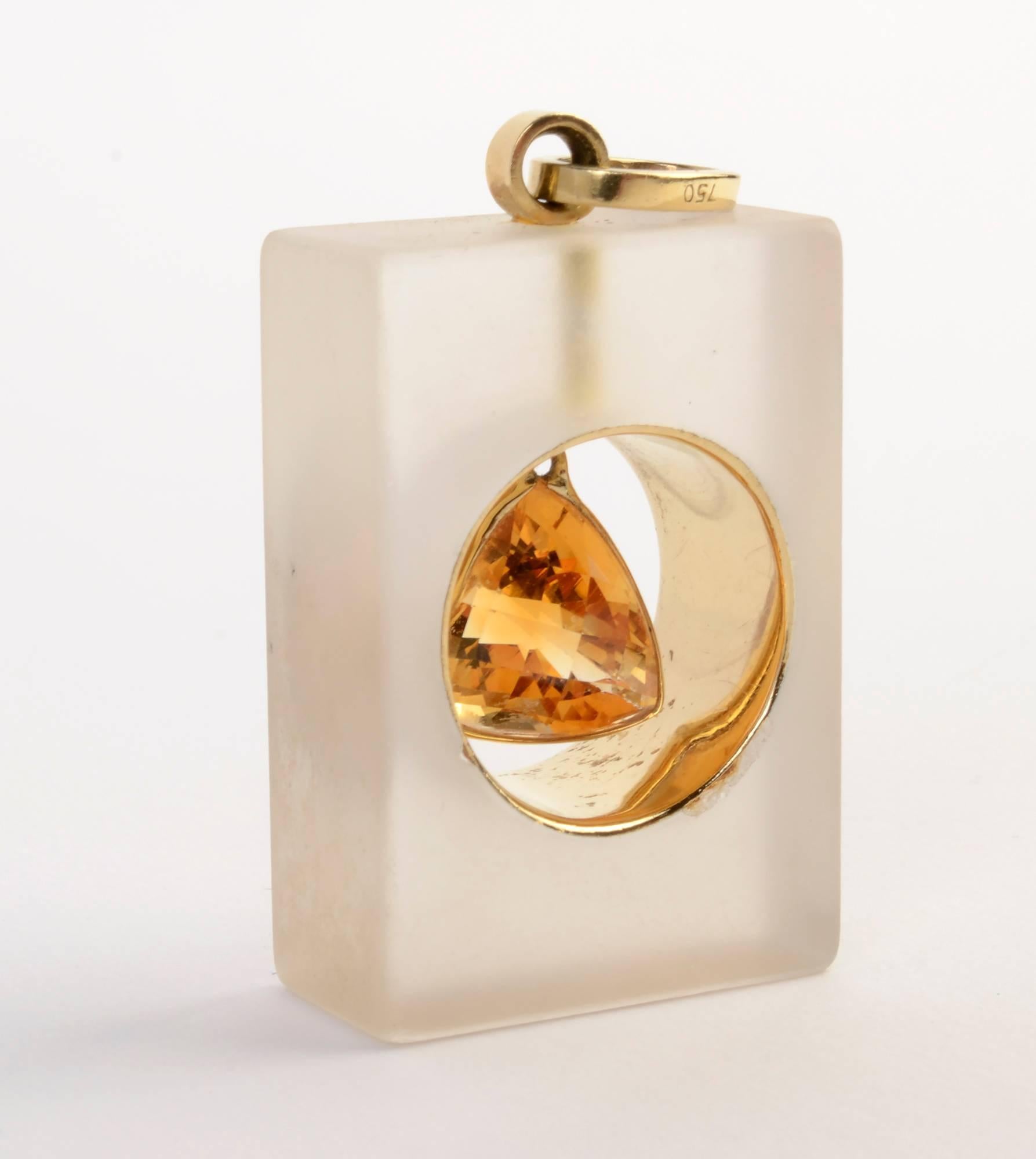 Unusual pendant in which a triangular, faceted citrine is suspended within a band of gold. The band is set within a rectangle of frosted crystal measuring 1 inch by 1.5 inches. The maker's name is signed on the hanging loop. I believe the name is
