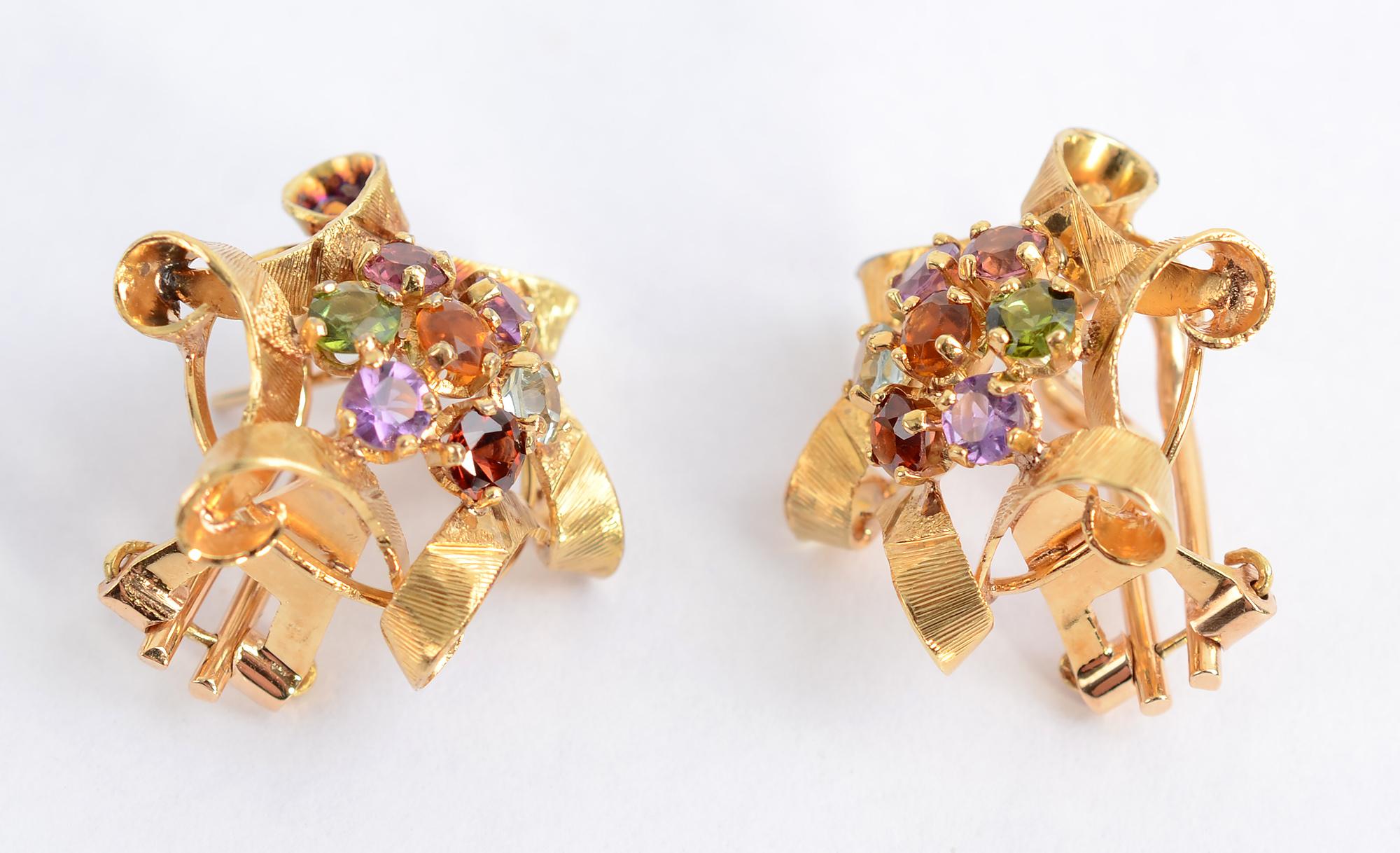 A cluster of multicolor gem earrings  look as though they are surrounded by gold looped ribbons. The seven stones in each earring include: amethyst; citrine; peridot; and blue topaz. The backs are clips with posts. The earrings are 7/8