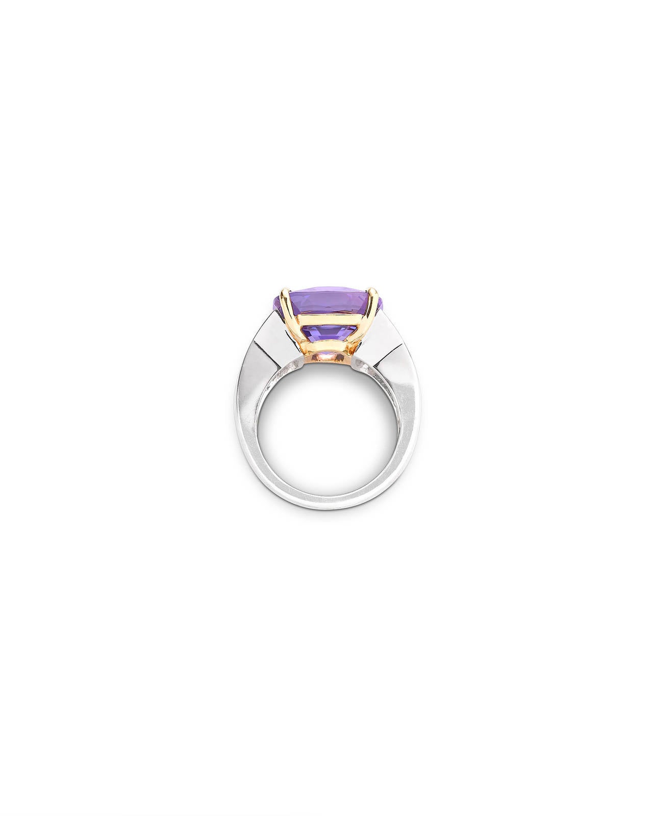 A brilliant 13.50-carat Natural Fancy lavender sapphire radiates at the center of this classically stunning ring. The step-cut gem is set in a sophisticated platinum and 18k yellow gold setting between glistening diamonds totaling 1.40 carats. Both
