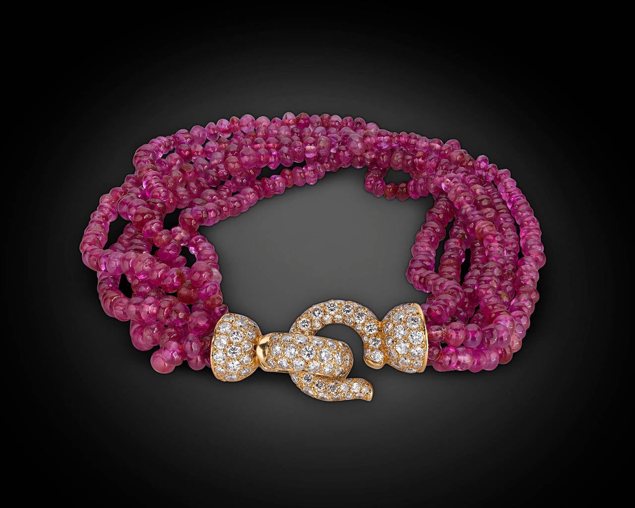 Six strands of wondrous red ruby beads take center stage in this exceptional Cartier bracelet. The 18K yellow gold hook clasp that secures this bracelet is enveloped in 2.50 carats of shimmering white diamonds. The legendary house of Cartier created
