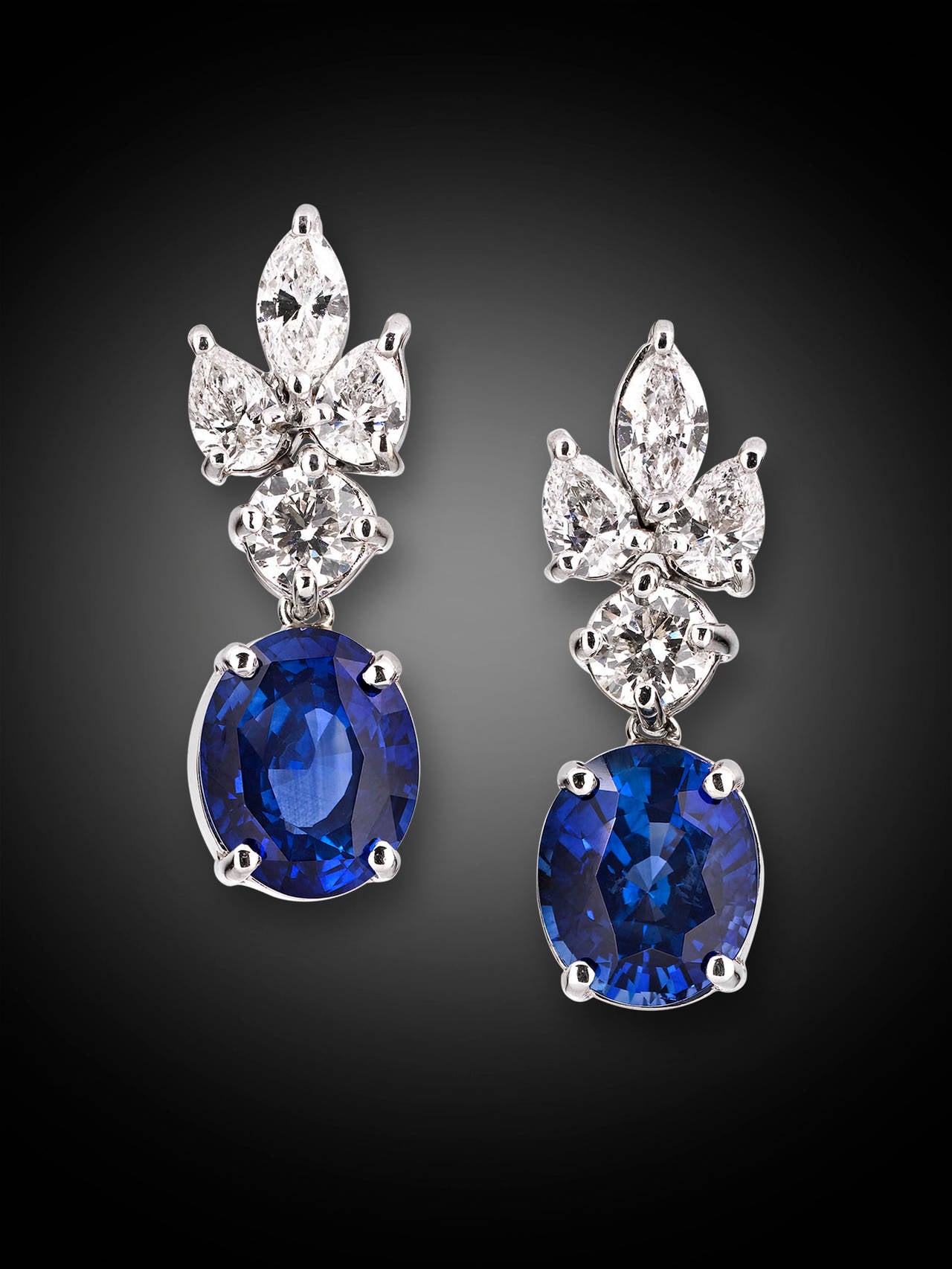 A pair of glorious blue oval sapphires dangle gracefully from these stylish and classic drop earrings. Weighing 8.20 total carats, these blue jewels are joined by 2.42 carats of marquise, pear and round-cut white diamonds in their 18K white gold