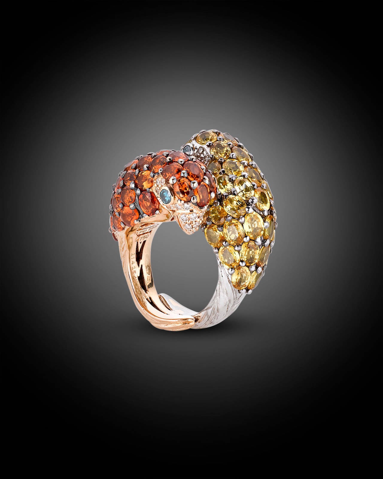 Glistening with the colors of a tropical sunset, this incredible bypass ring by Zorab Atelier de Creation takes the form of a pair of parrots brought to life by dazzling yellow and orange sapphires. Crafted of 18K gold, this incredible ring is set