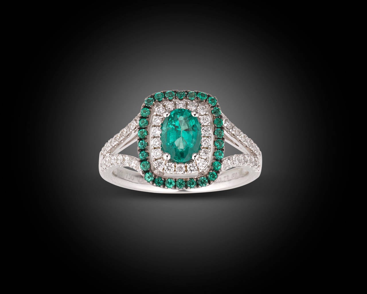 A brilliant 0.90 carat emerald radiates at the center of this enchanting and feminine  ring. The gorgeous colored gemstone is perfectly accented by fifty shimmering diamonds totaling 0.46 carats and twenty-six additional emeralds totaling 0.18