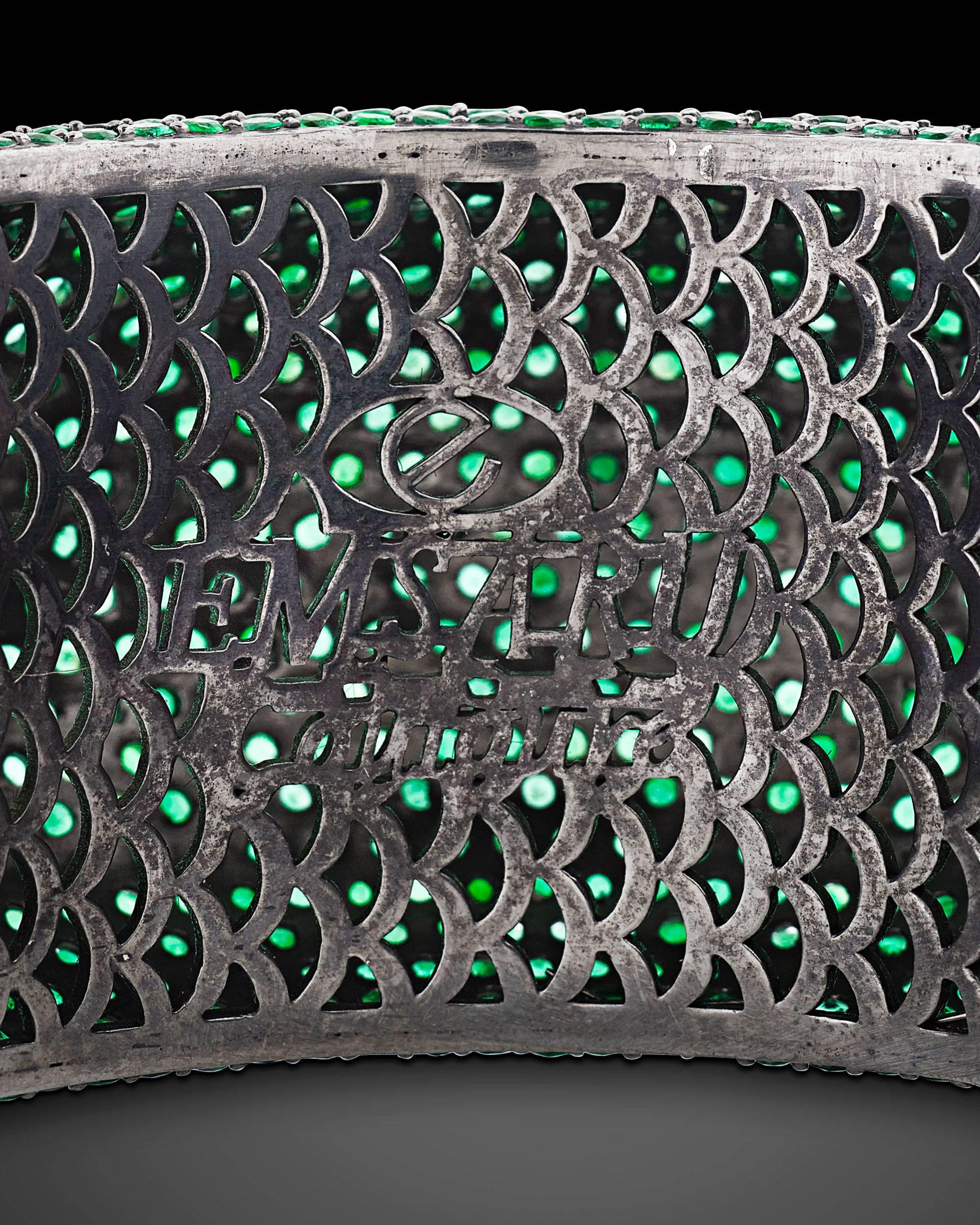 A field of dazzling emerald green envelops this sophisticated and bold bangle bracelet. Approximately 115 total carats of emeralds blanket the design, beautifully blended within the rhodium blackened sterling silver setting. Gently rounded, the