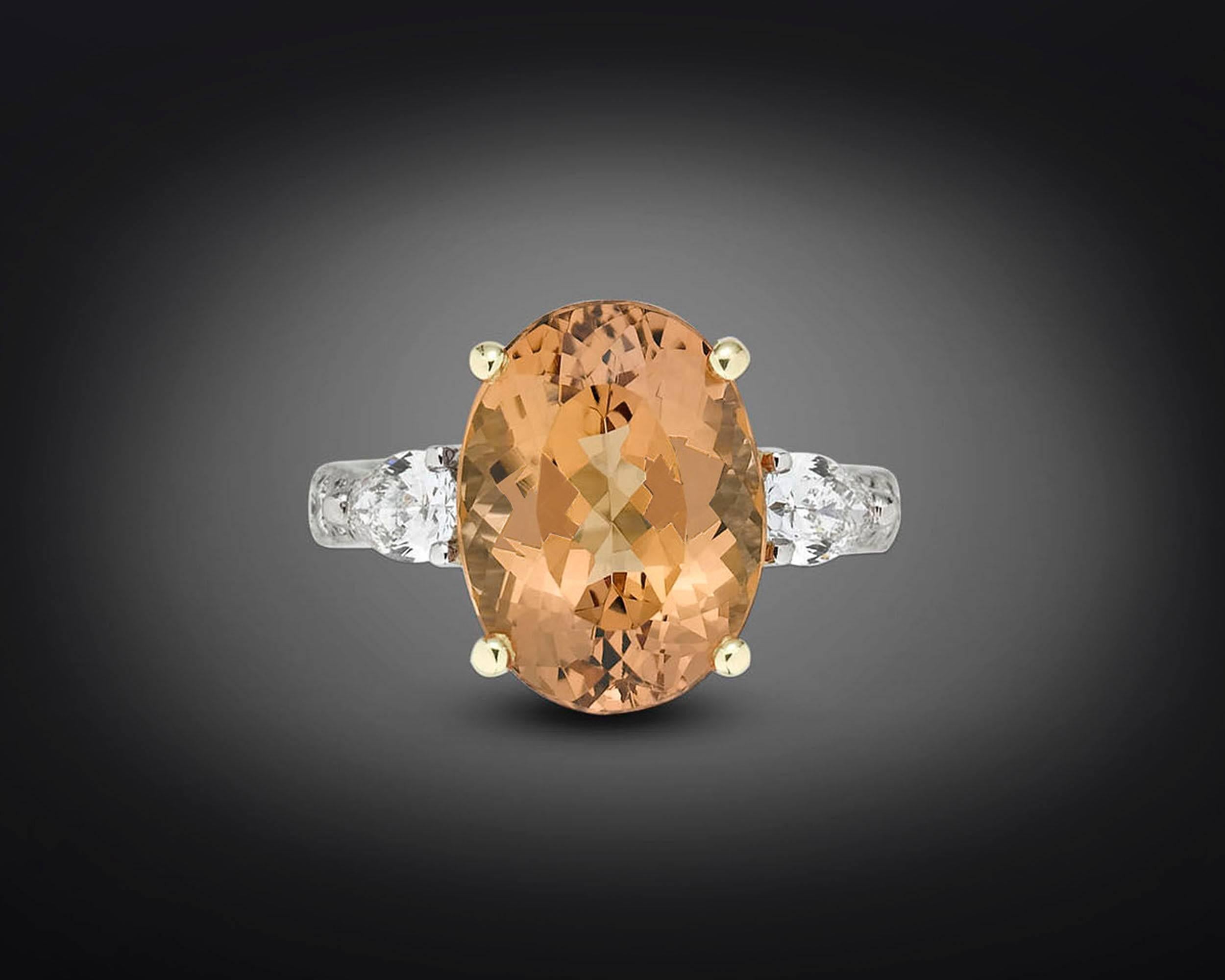With an exceptional peachy hue reminiscent of a tropical sunset, this 6.63 carat Imperial topaz is one of the most sought-after colored gemstones. This elegant oval specimen is flanked by a pair of pear-shaped diamonds totaling .49 carats, with