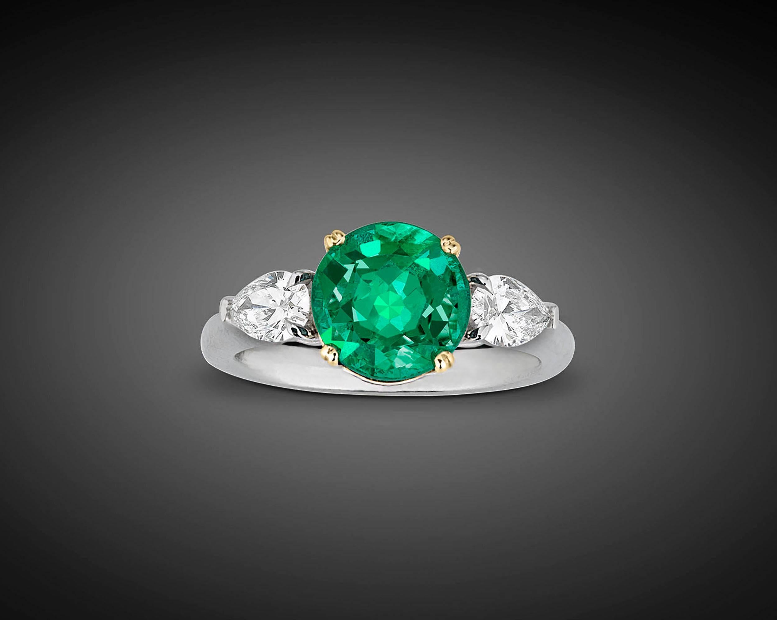 A stunning 2.58-carat emerald takes center stage in this exquisite ring. The luminous round brilliant-cut gem is perfectly complemented by two pear-cut white diamonds weighing 0.61 total carats, which support it on either side.  Displaying vibrant