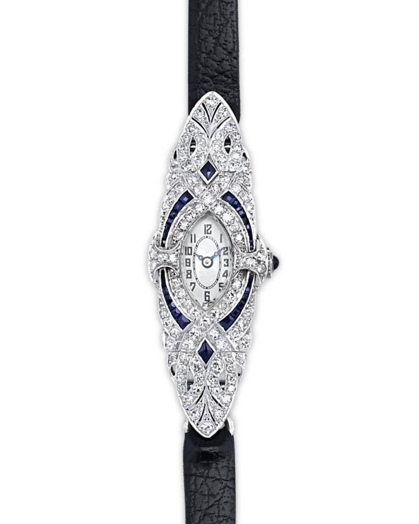 This spectacular ladies' wristwatch embodies the sleek and stylish spirit of Art Deco design. The platinum timepiece is embedded with a swirling array of colorless diamonds, while rich, royal blue sapphires add a hint of drama to the design. At the
