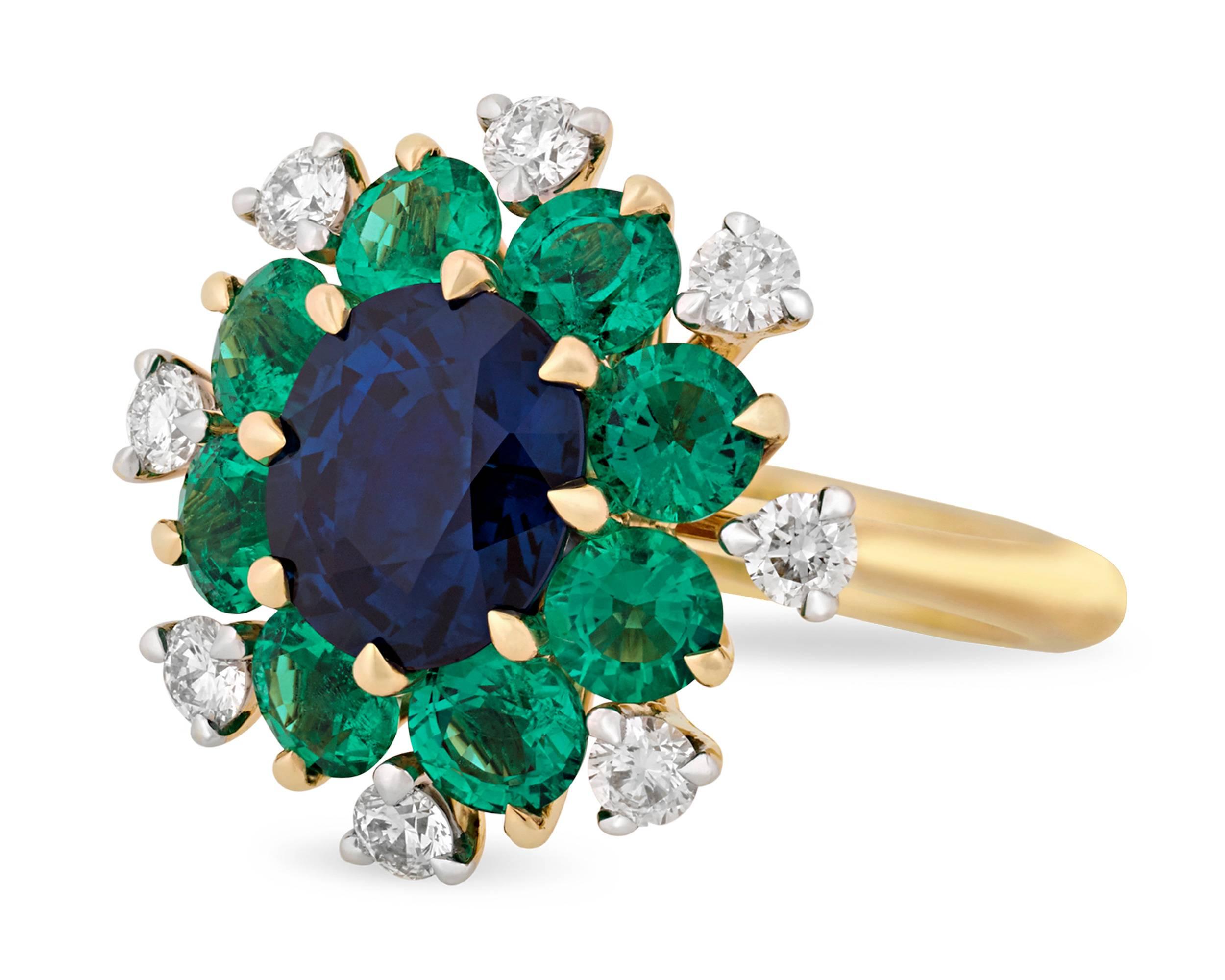 The unmistakable beauty of sapphires and emeralds distinguish this elegant ring. Designed to resemble a flower, this 18K gold ring is centered by a 2.56-carat rich blue sapphire encircled by eight green emeralds totaling 1.93 carats and eight white