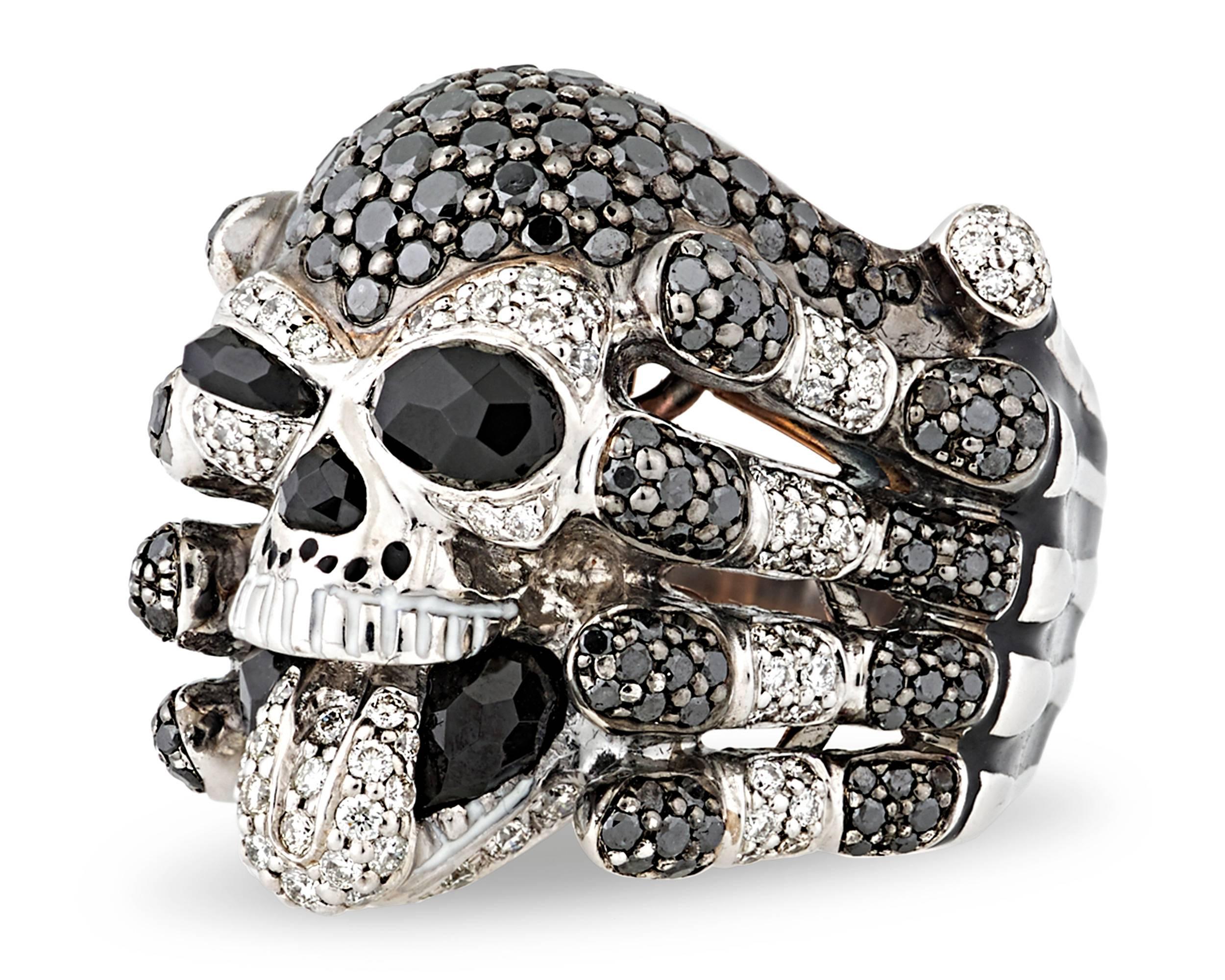 A cheeky skull sticks out his diamond-encrusted tongue in this beautifully macabre ring. Held aloft by a band crafted in the form of skeletal hands, the skull is set with 2.92 total carats of spinels in its eyes, nose, and mouth. Black diamonds