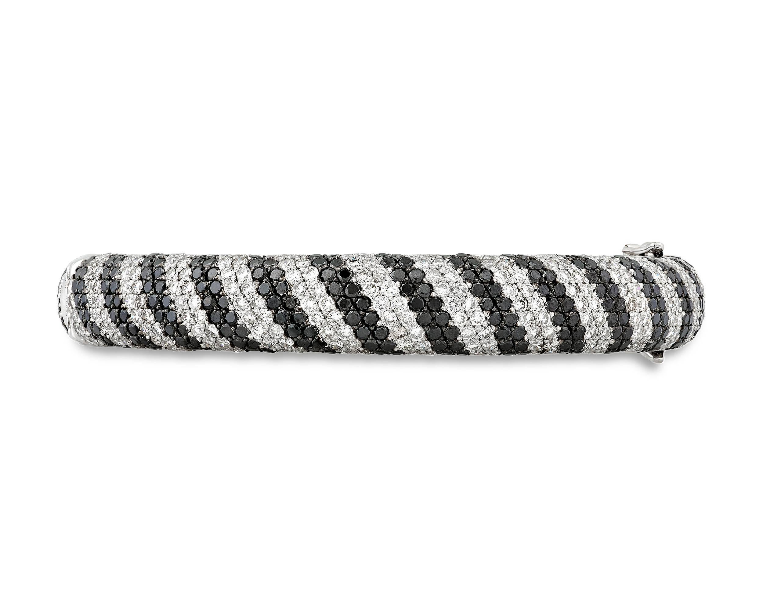 This elegant black and white diamond bangle bracelet boasts a sophisticated and streamlined design. Rows of black diamonds weighing approximately 9.94 total carats alternate with approximately 9.94 total carats of white diamonds in a bold stripe