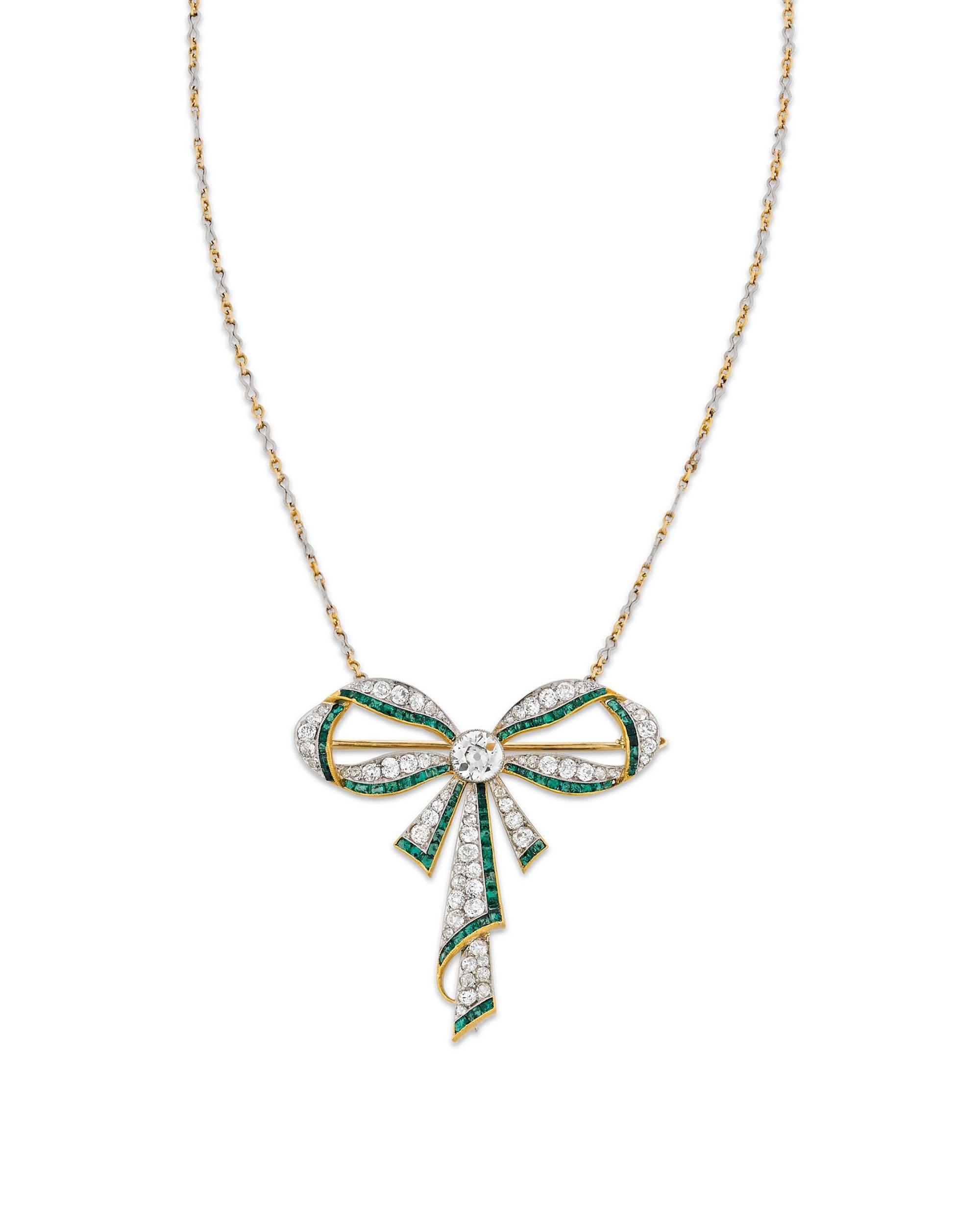 This sensational Edwardian pendant necklace showcases an exquisite design illuminated by extraordinary stones. Dazzling colorless diamonds adorn the charming 18k yellow gold and platinum bow form, while verdant emeralds add dramatic detail to the
